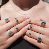 Close-up of hands wearing multiple emerald green gemstone rings on a neutral background