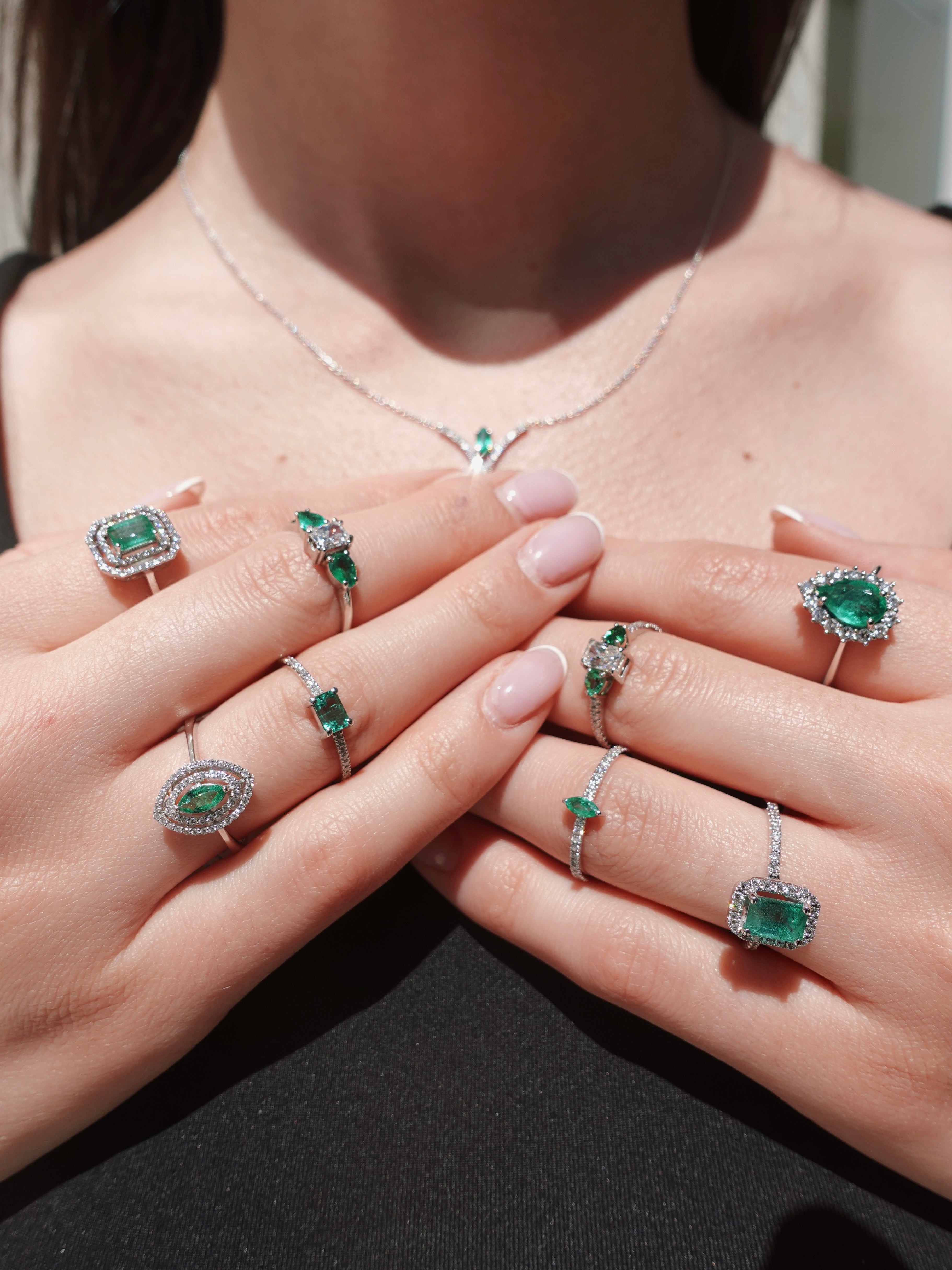 Close-up of hands wearing multiple emerald green gemstone rings on a neutral background