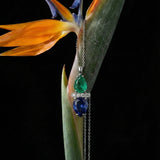 Jewelry with emerald and sapphire stones hanging from a bird of paradise flower against a black background