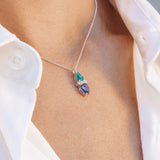 Necklace with sapphire and emerald with a pendant worn by a person wearing a white shirt.