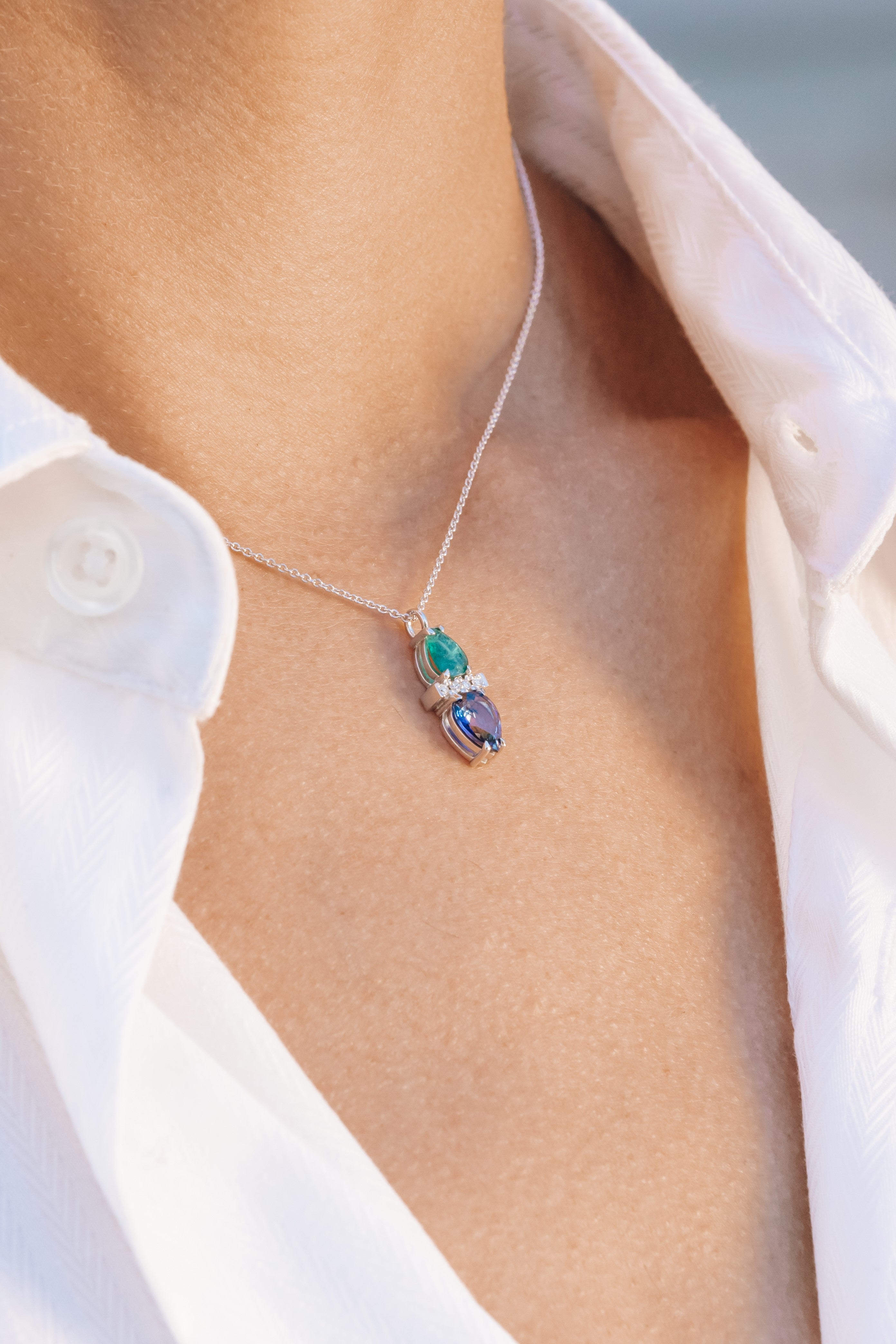 Necklace with sapphire and emerald with a pendant worn by a person wearing a white shirt.