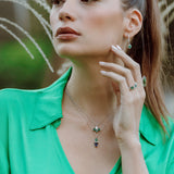 Woman wearing emerald and sapphire dup drop pendent against a natural background