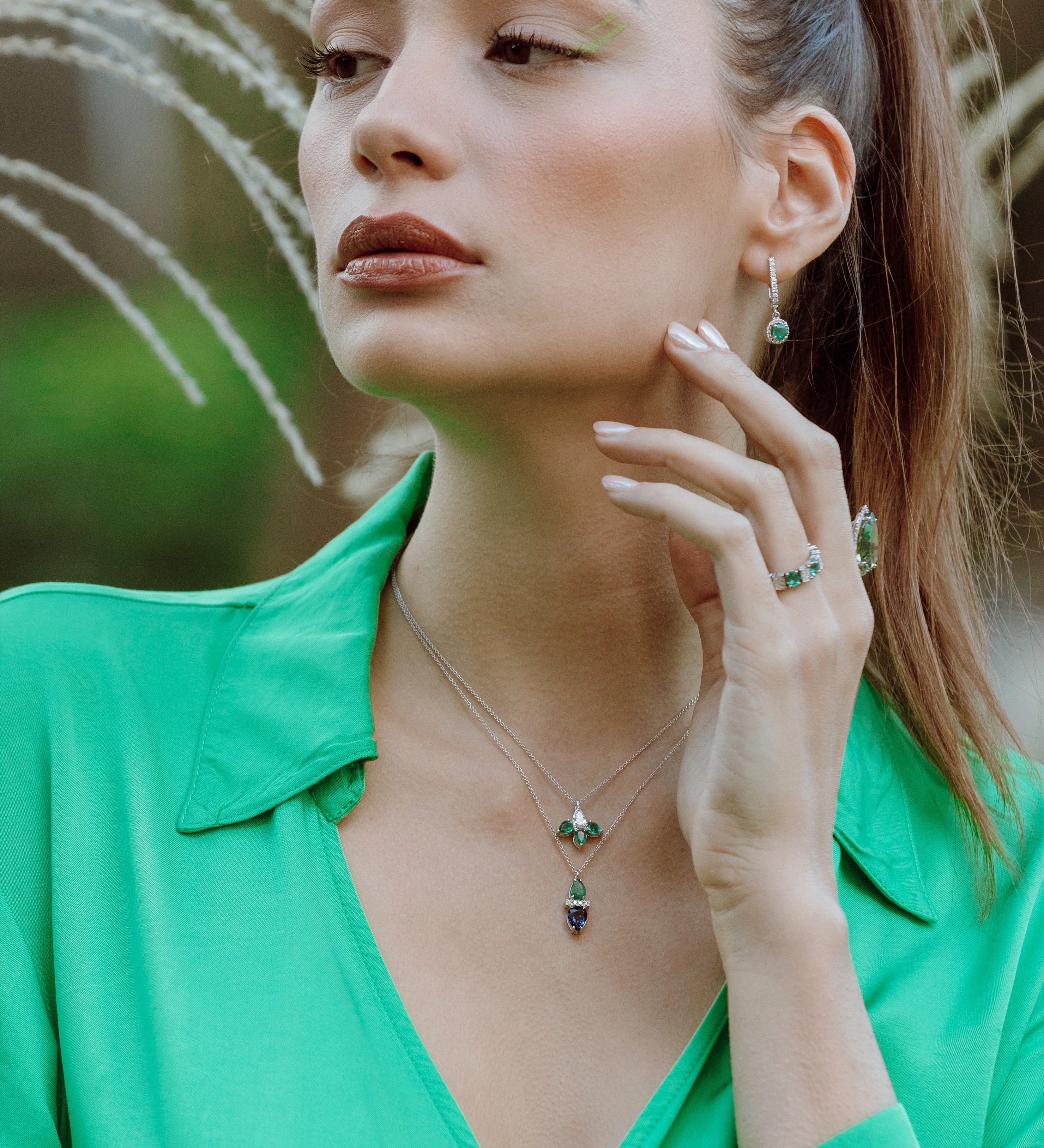 Woman wearing emerald and sapphire dup drop pendent against a natural background