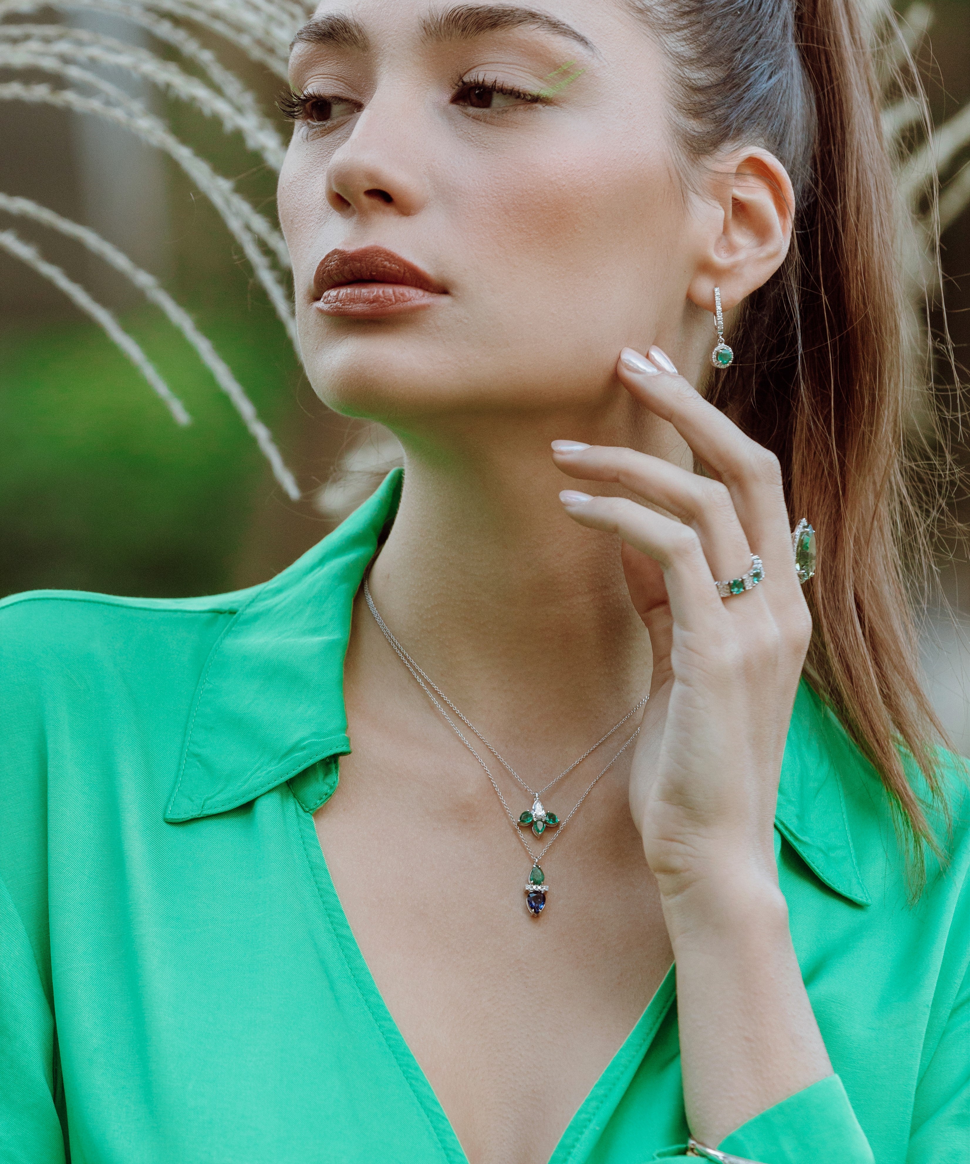 Woman wearing emerald and sapphire dup drop pendent against a natural background