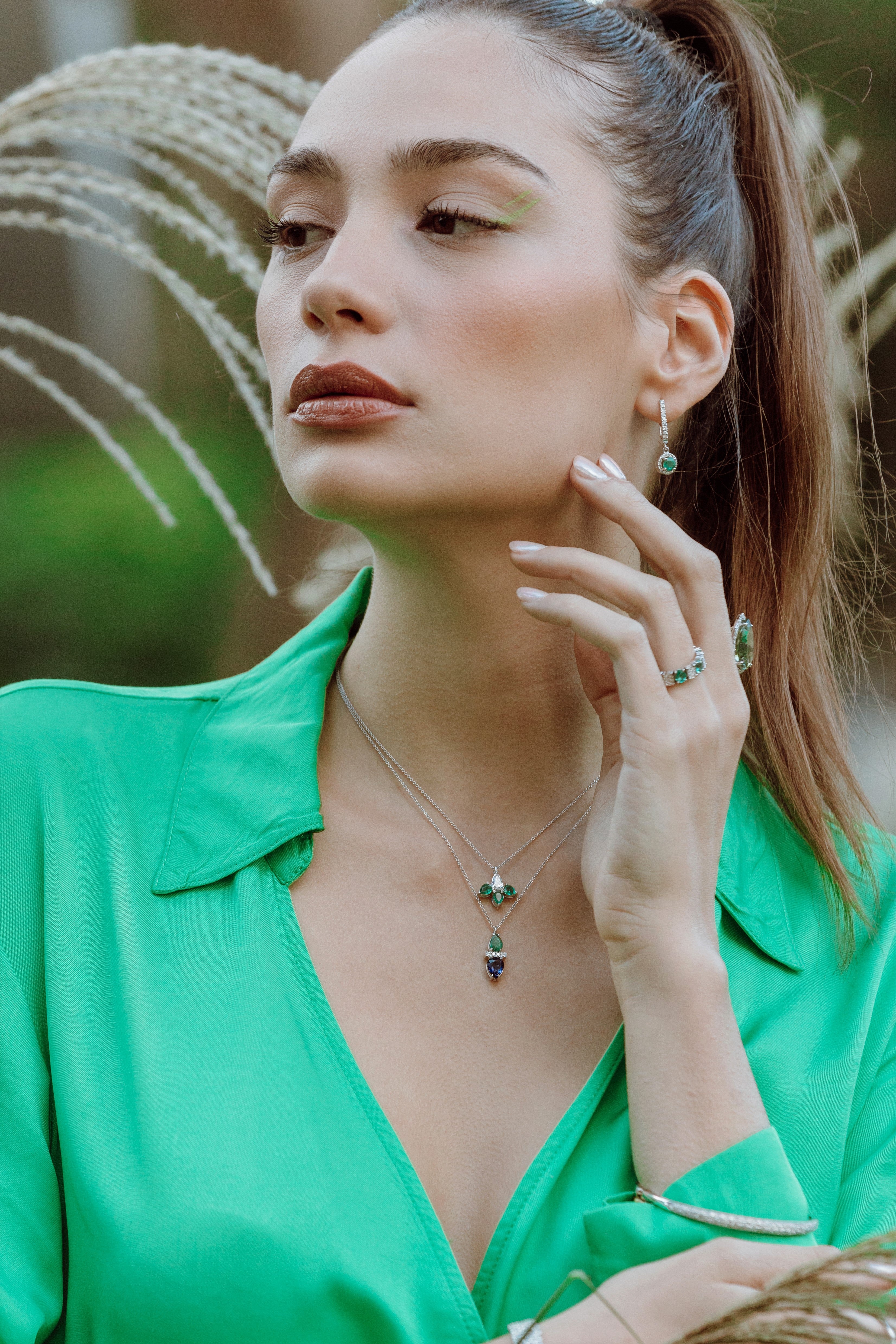 Woman wearing emerald and sapphire dup drop pendent against a natural background