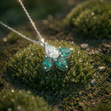 White gold necklace with three emeralds and one diamond on a mossy surface