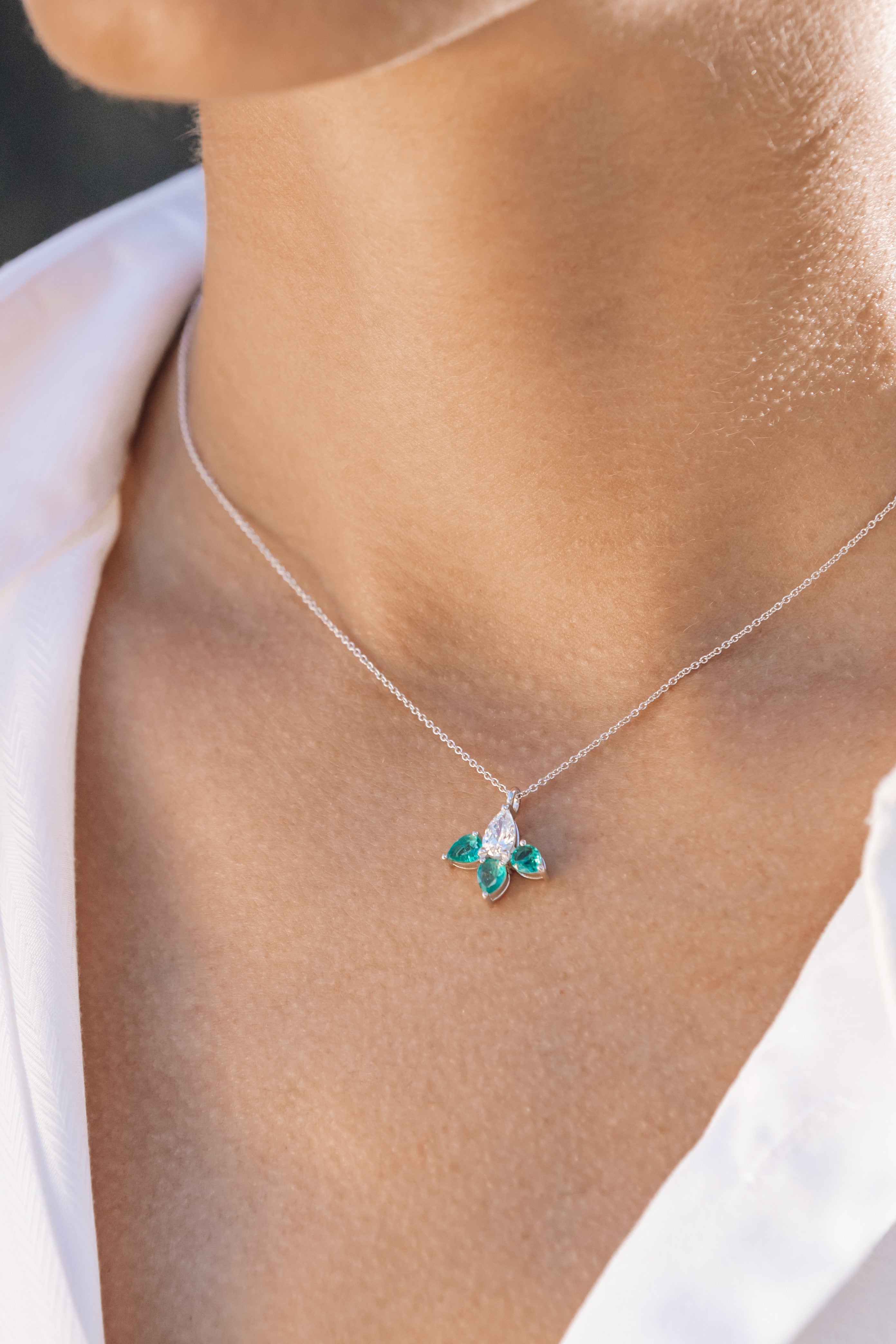Necklace with a pendant featuring green gemstones worn by a person.