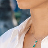 Necklace with an emerald and diamond pendant worn by a person against a blurred outdoor background