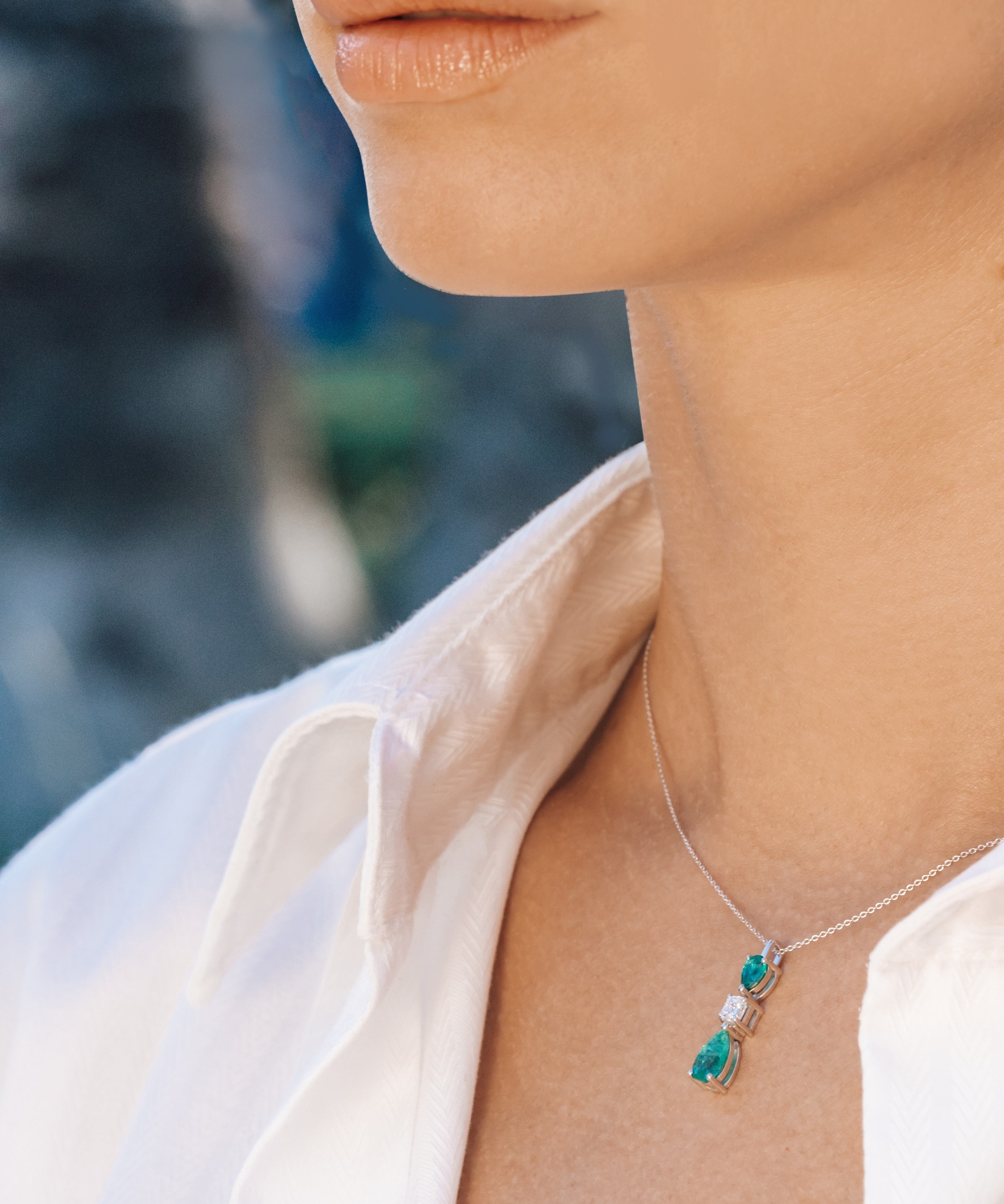 Necklace with an emerald and diamond pendant worn by a person against a blurred outdoor background