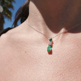 Close-up of a necklace with a green pendant on a person's neck against a blurred outdoor background.