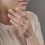 Close-up of a woman's hand wearing a ring with emeralds and diamond, touching her face.