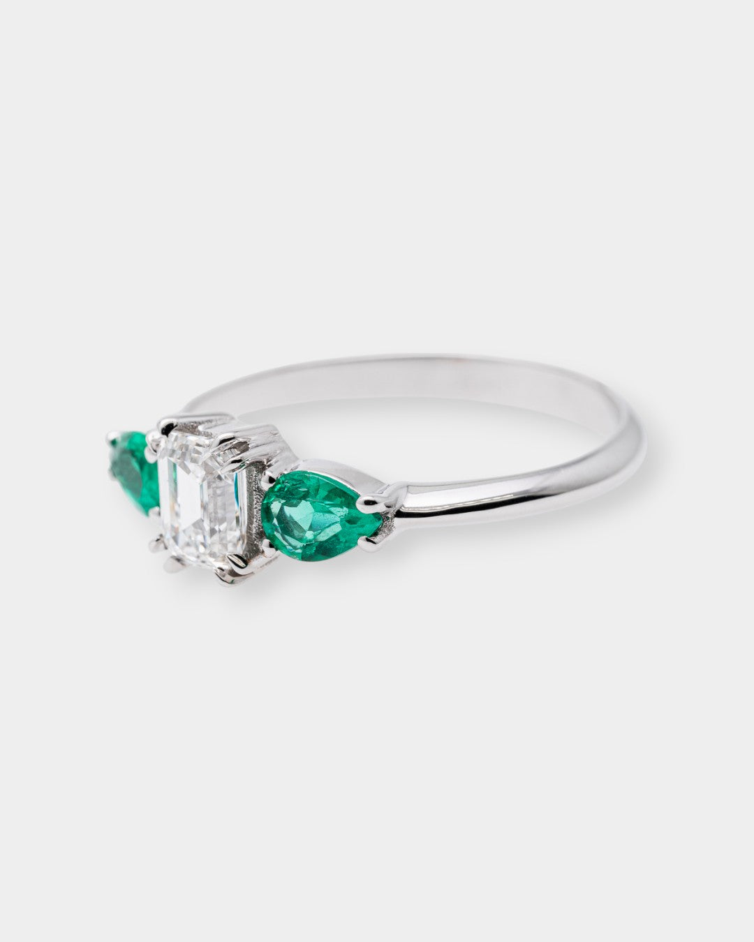 white gold ring with a central diamond and two emeralds on a white background
