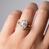 A close-up of a hand wearing a gold engagement ring with a round brilliant-cut diamond and a matching diamond-accented band.