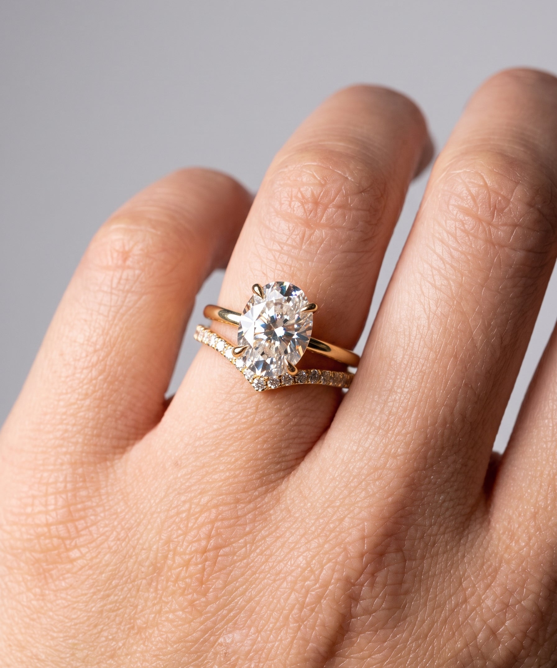A close-up of a hand wearing a gold engagement ring with a round brilliant-cut diamond and a matching diamond-accented band.