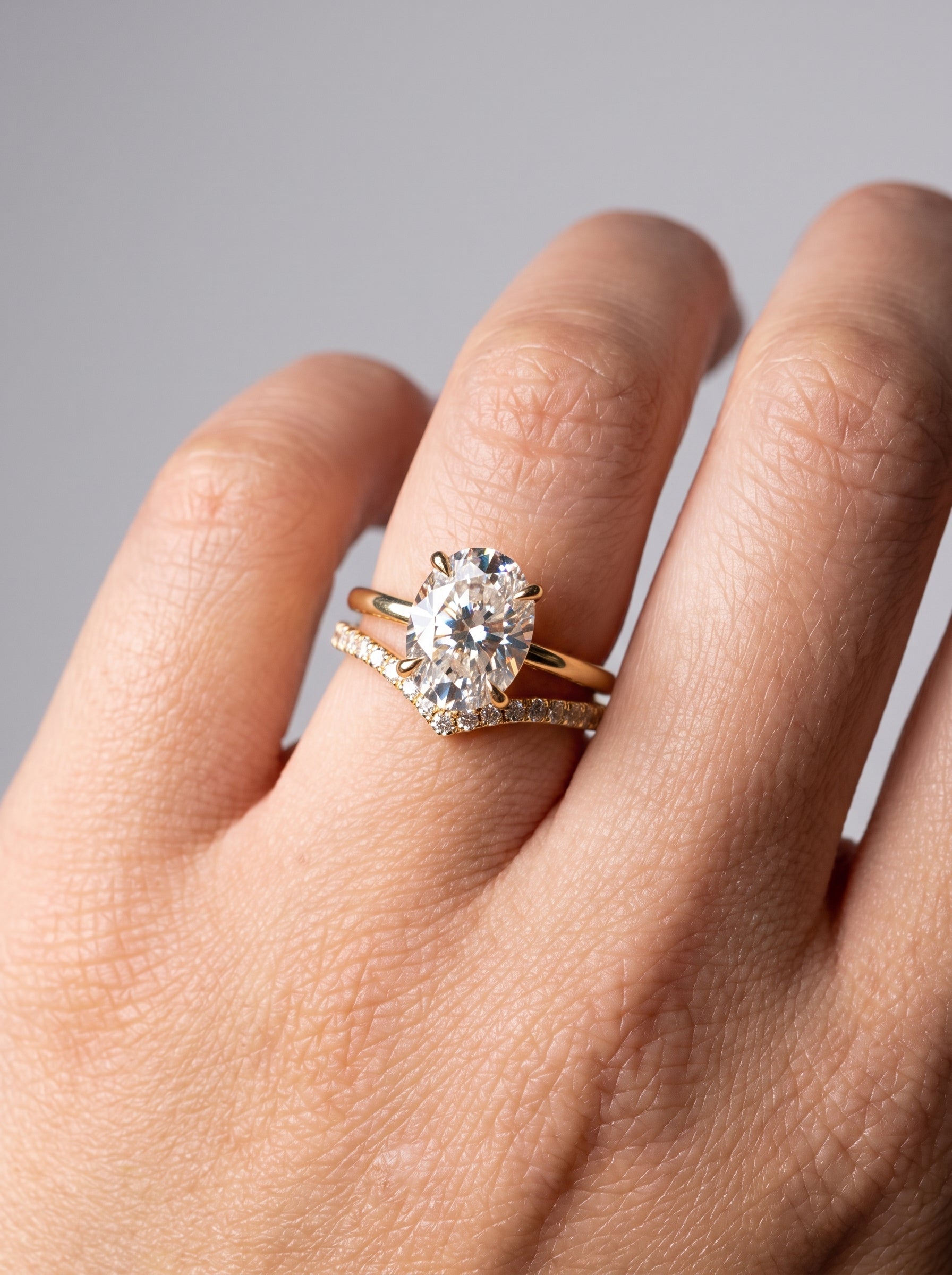 A close-up of a hand wearing a gold engagement ring with a round brilliant-cut diamond and a matching diamond-accented band.