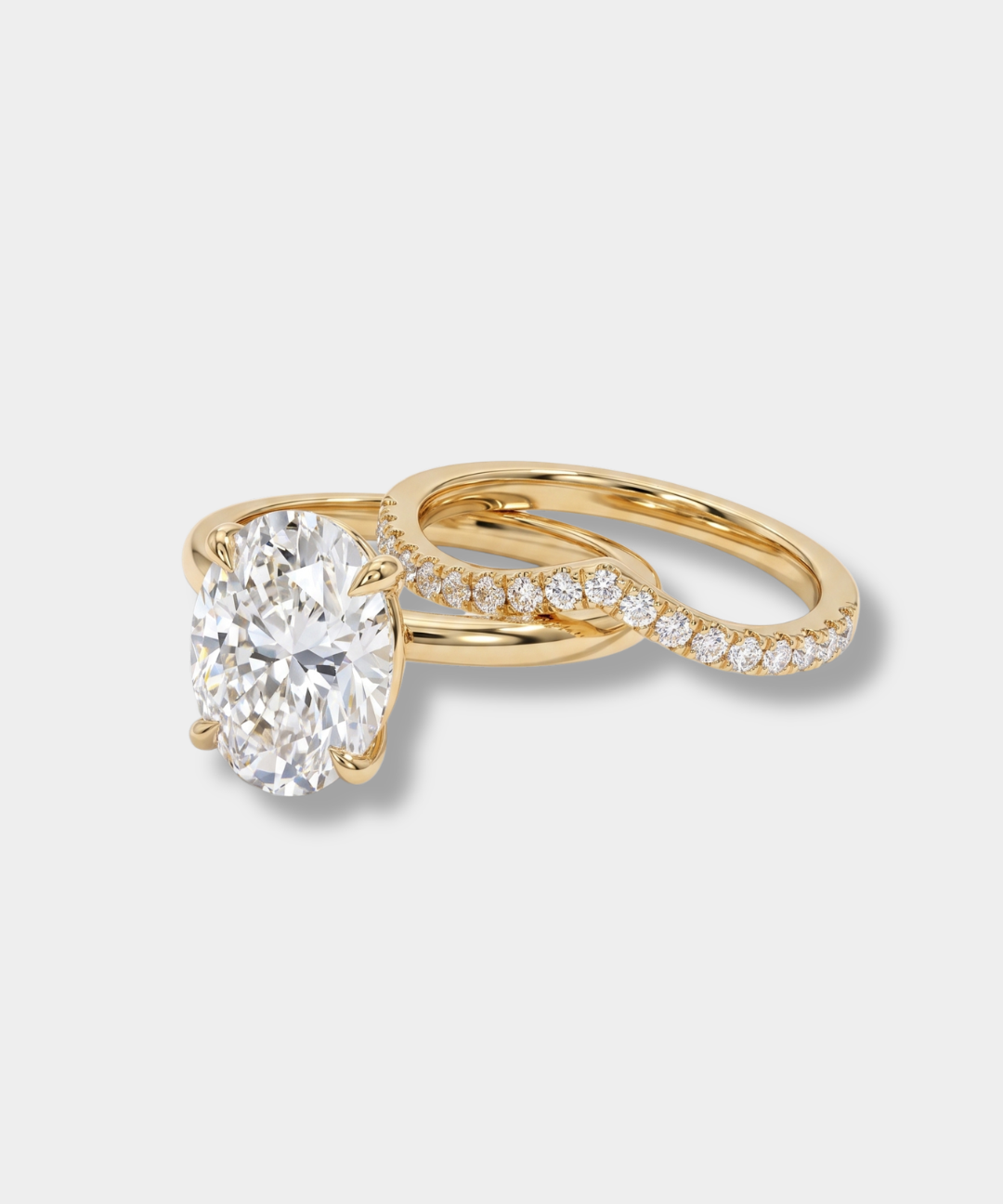 A yellow gold engagement ring featuring a large oval-cut diamond center stone, with a twisted pavé band accented by small round diamonds, set against a light gray background.
