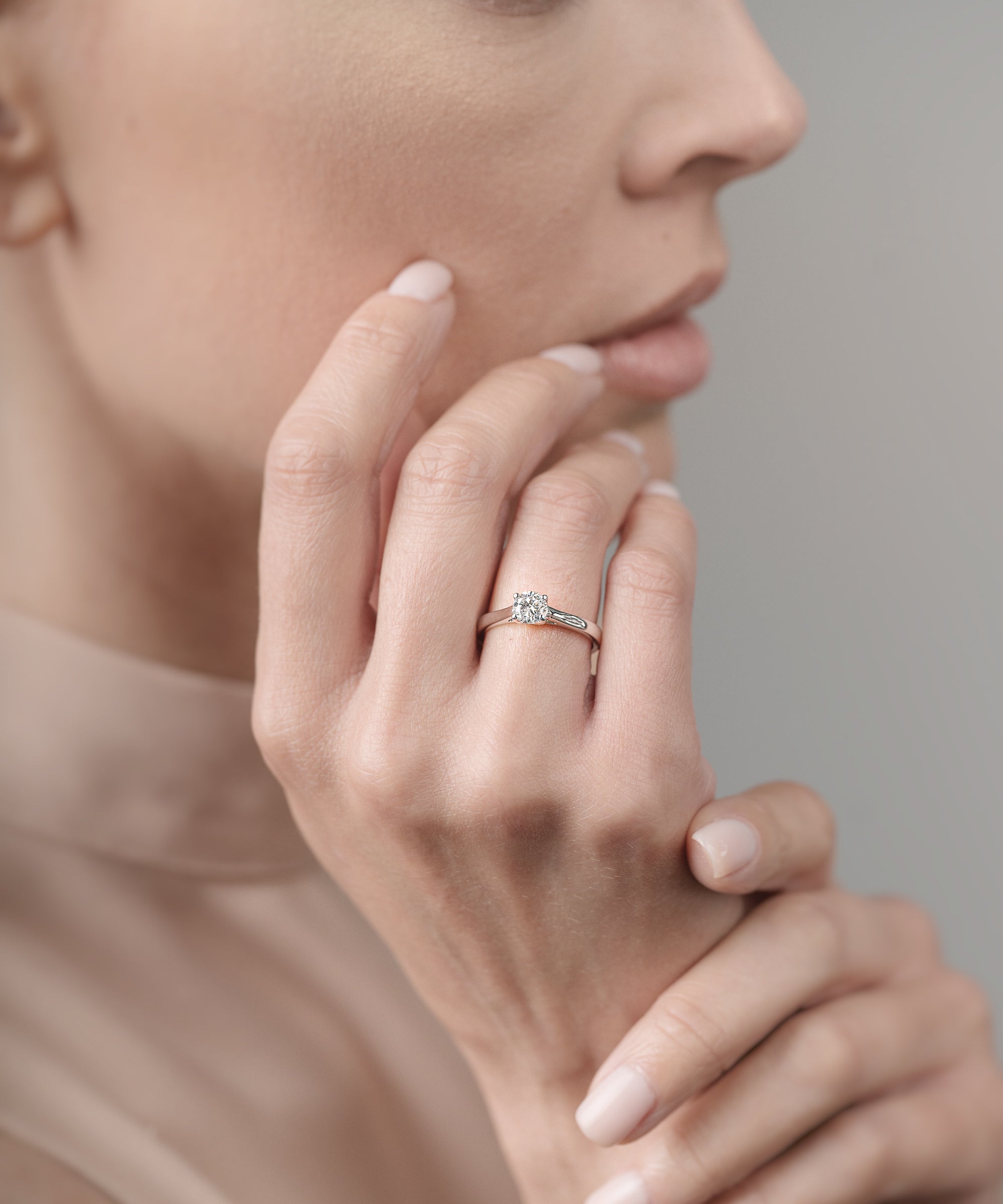 Close-up of a woman's hand with a ring on her finger, touching her face.