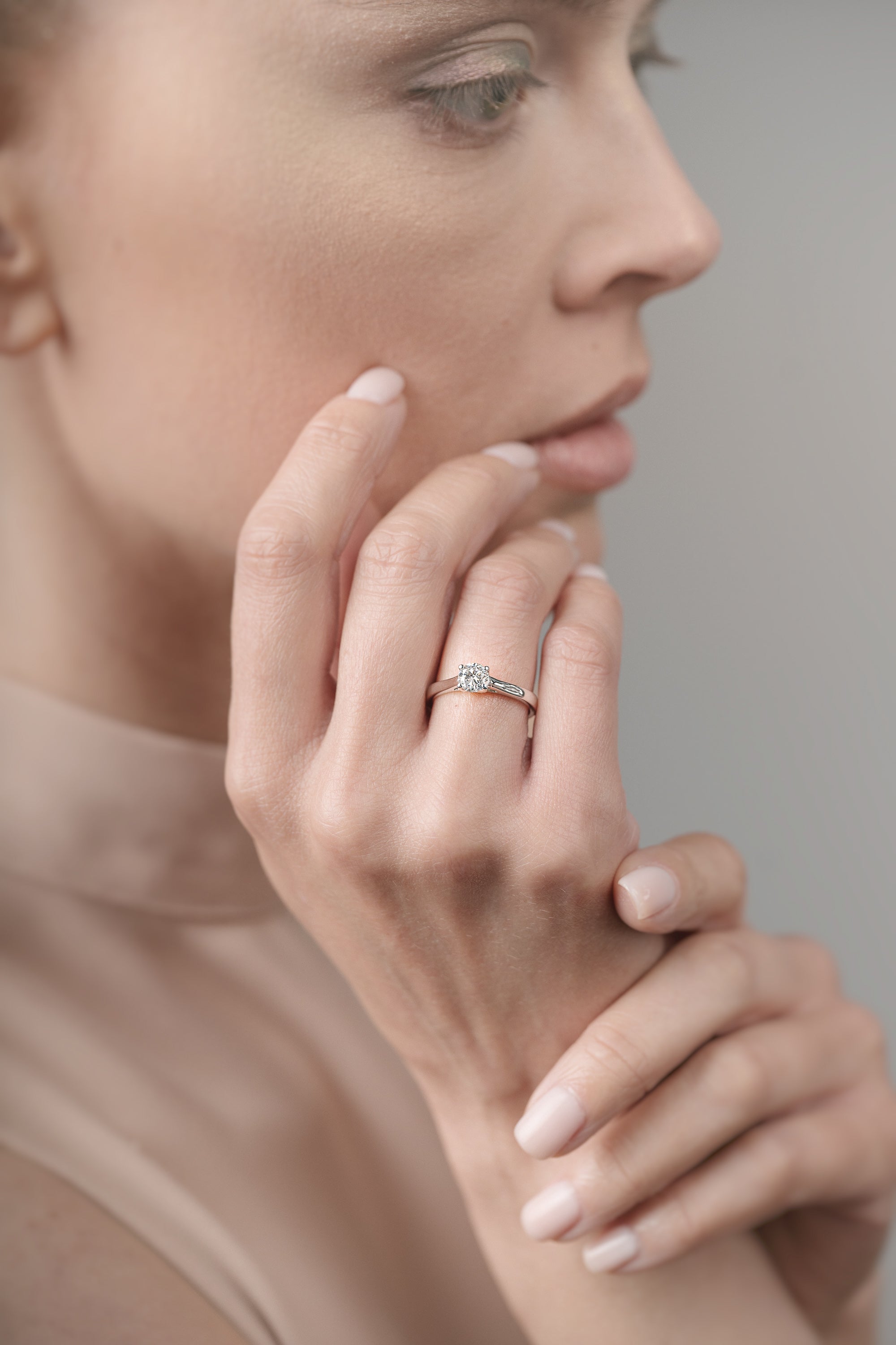 Close-up of a woman's hand with a ring on her finger, touching her face.