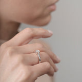Close-up of a hand wearing a white gold ring with a diamond on a neutral background