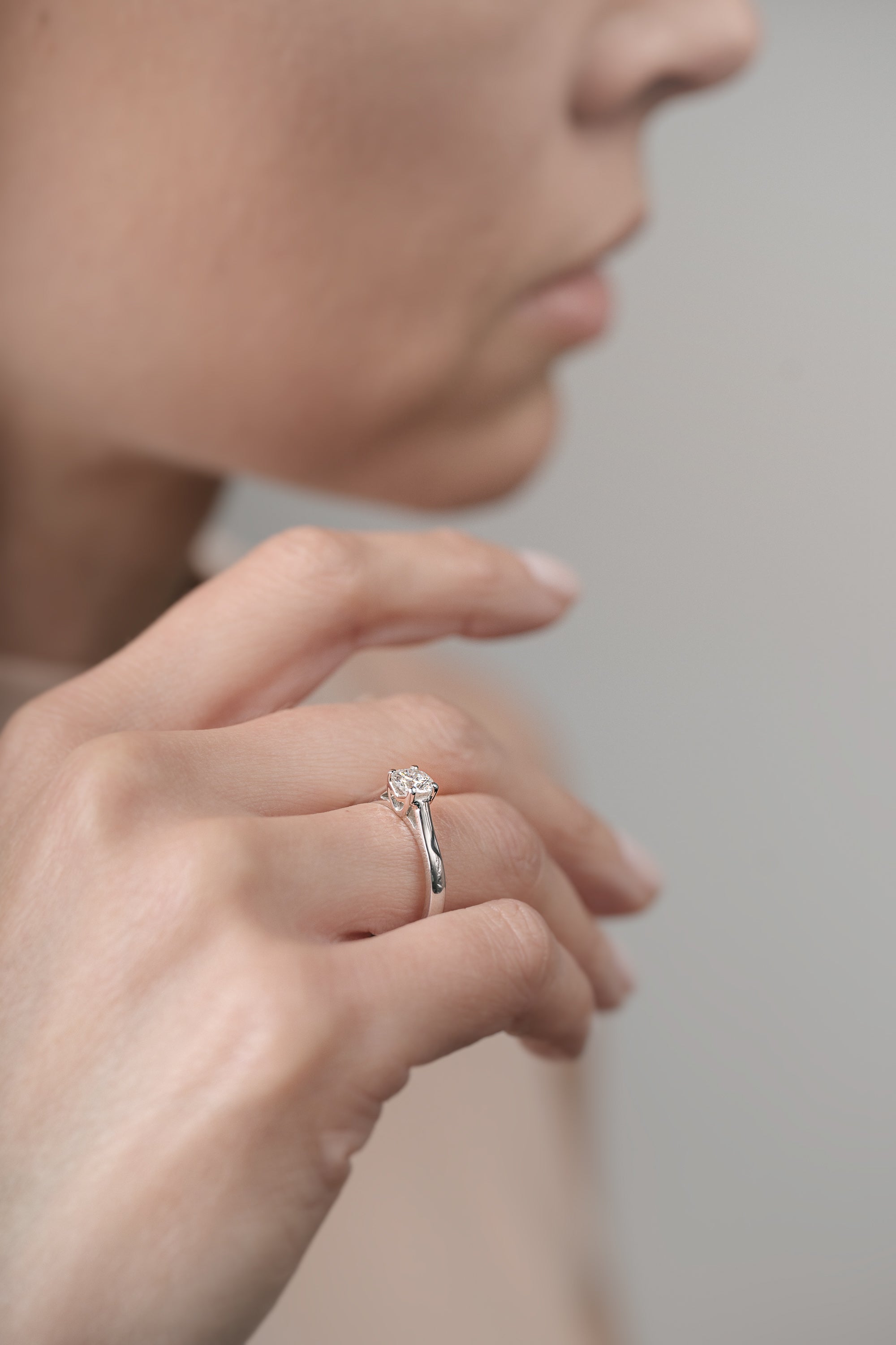 Close-up of a hand wearing a white gold ring with a diamond on a neutral background