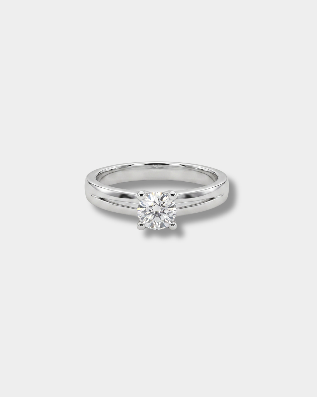 A classic solitaire engagement ring featuring a round brilliant-cut diamond set in a polished silver-colored band, shown against a neutral light gray background.