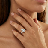 Close-up of a woman's hand wearing a marquise-cut diamond ring on her finger, with a soft focus on her face.