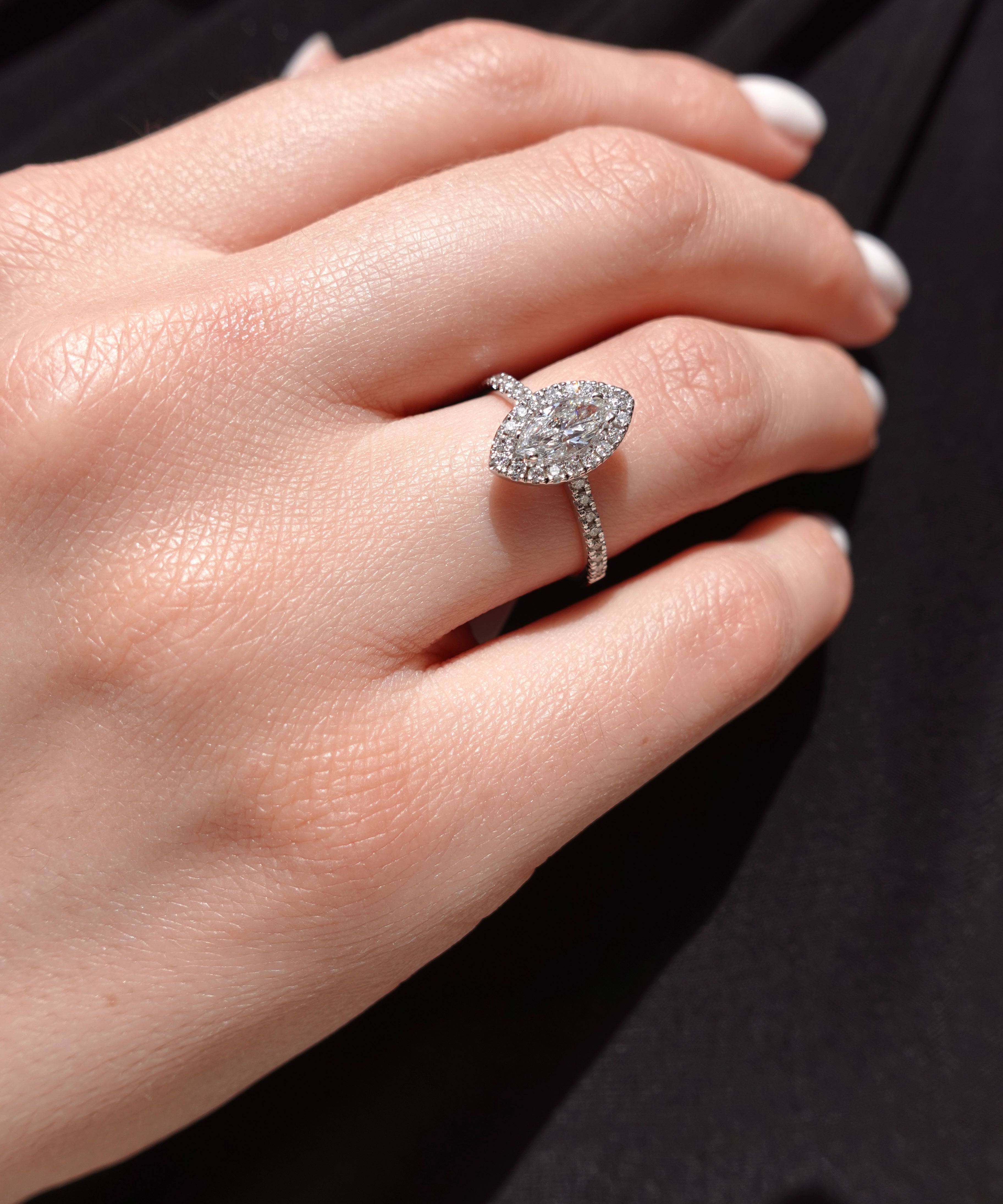 Close-up of a hand wearing a diamond ring with marquise-shaped center stone on a dark background