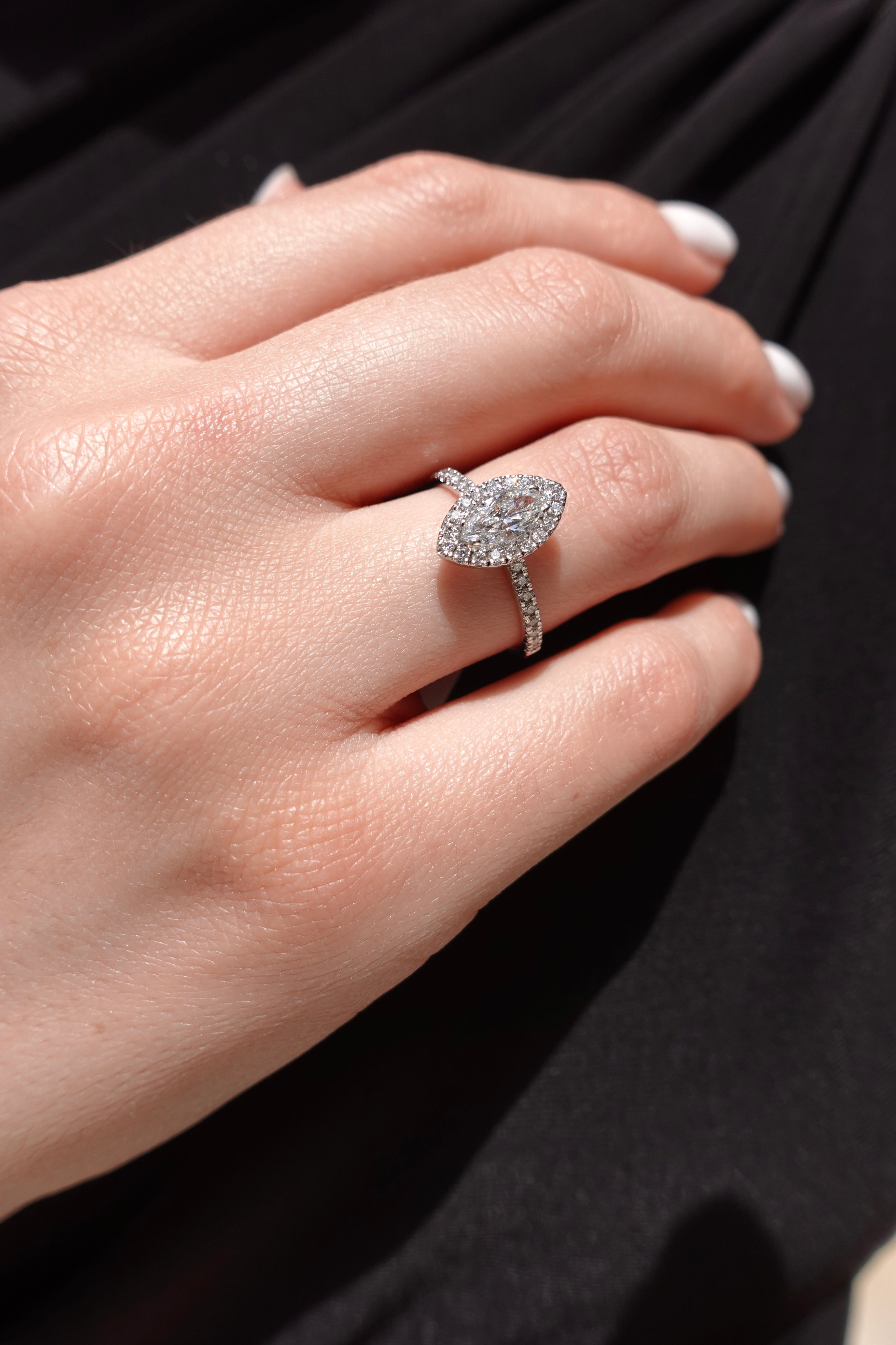 Close-up of a hand wearing a diamond ring with marquise-shaped center stone on a dark background