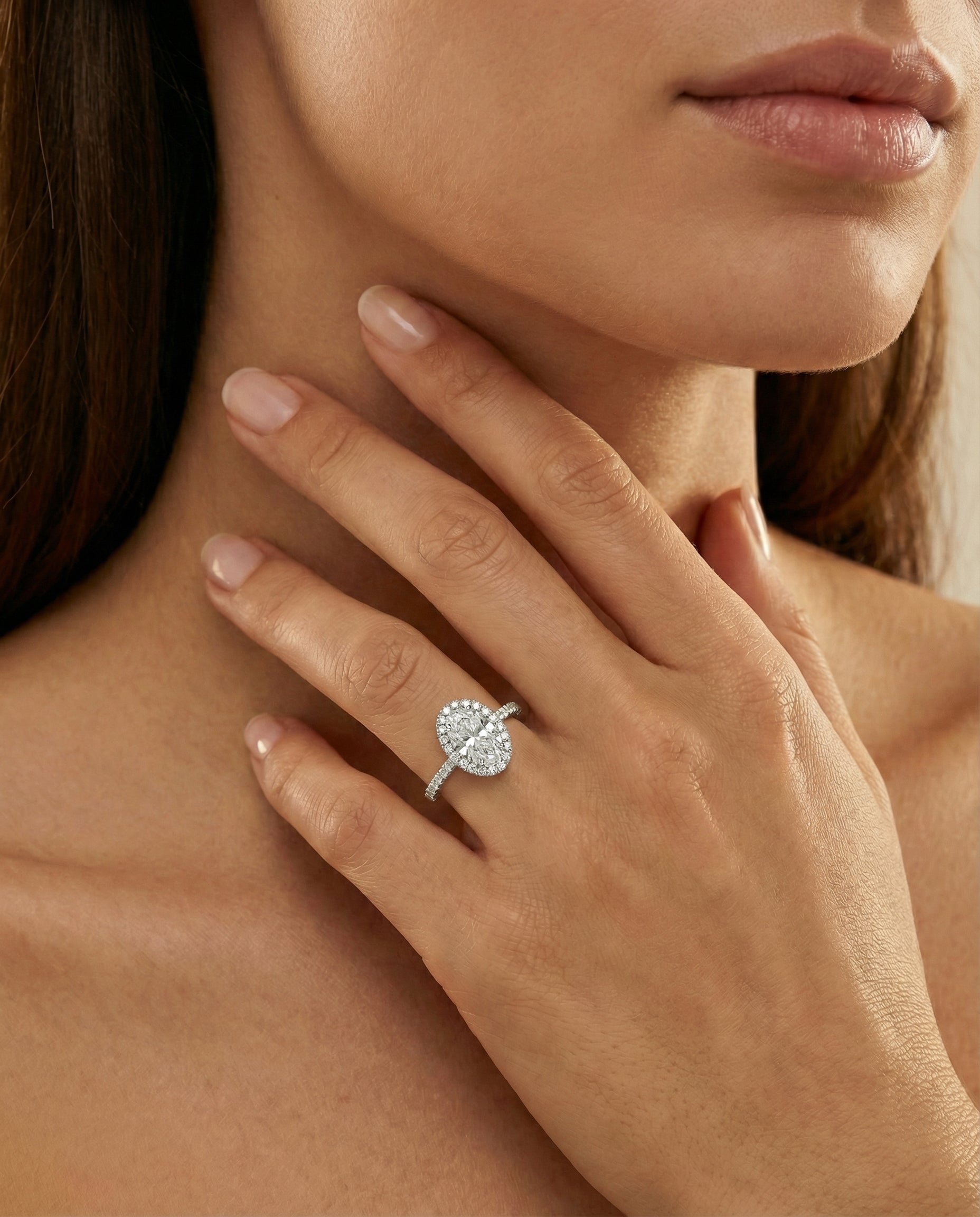 A model's hand wearing an oval-cut diamond halo engagement ring 