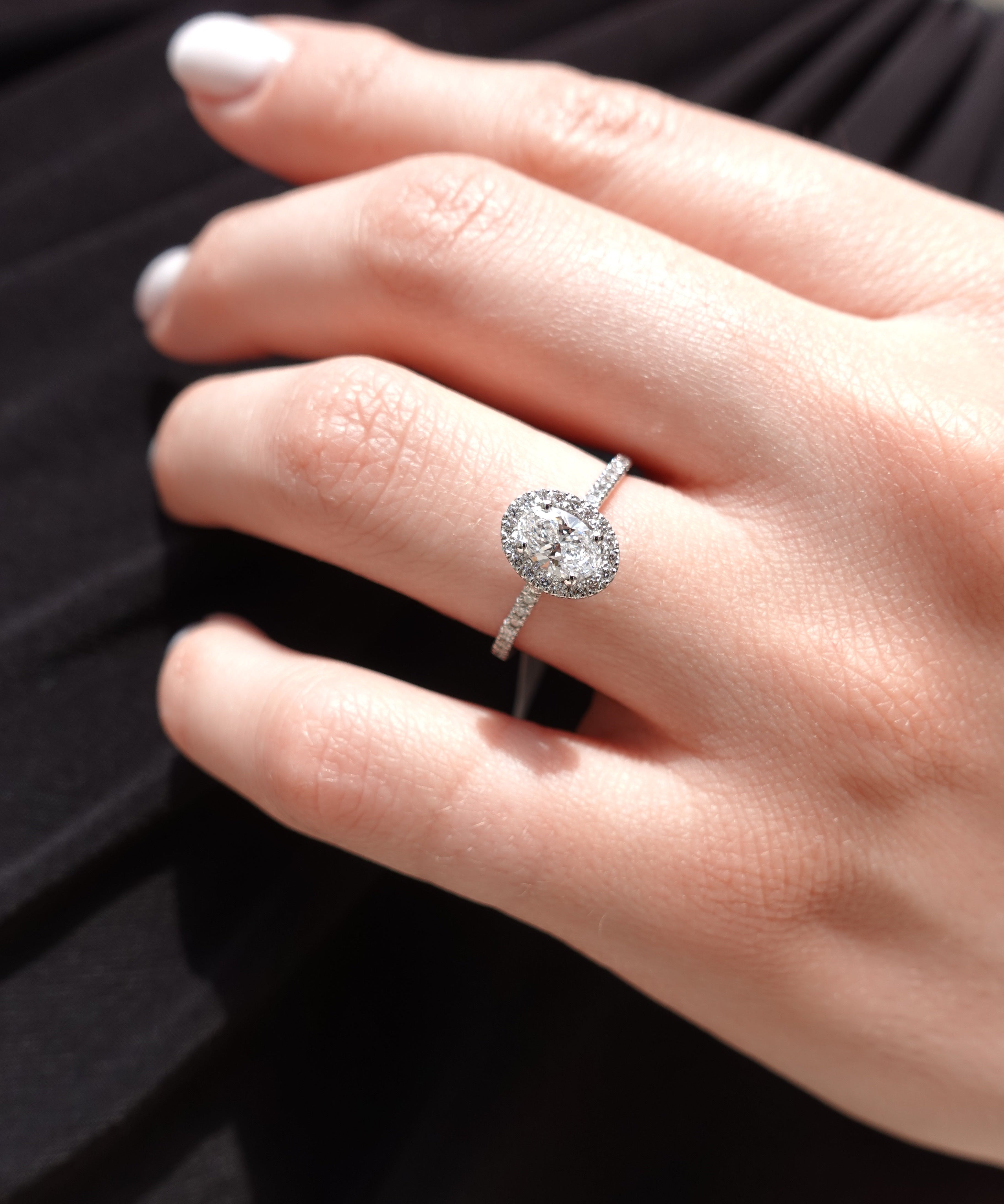 Close-up of a hand wearing a oval-cut diamond ring with a blurred background