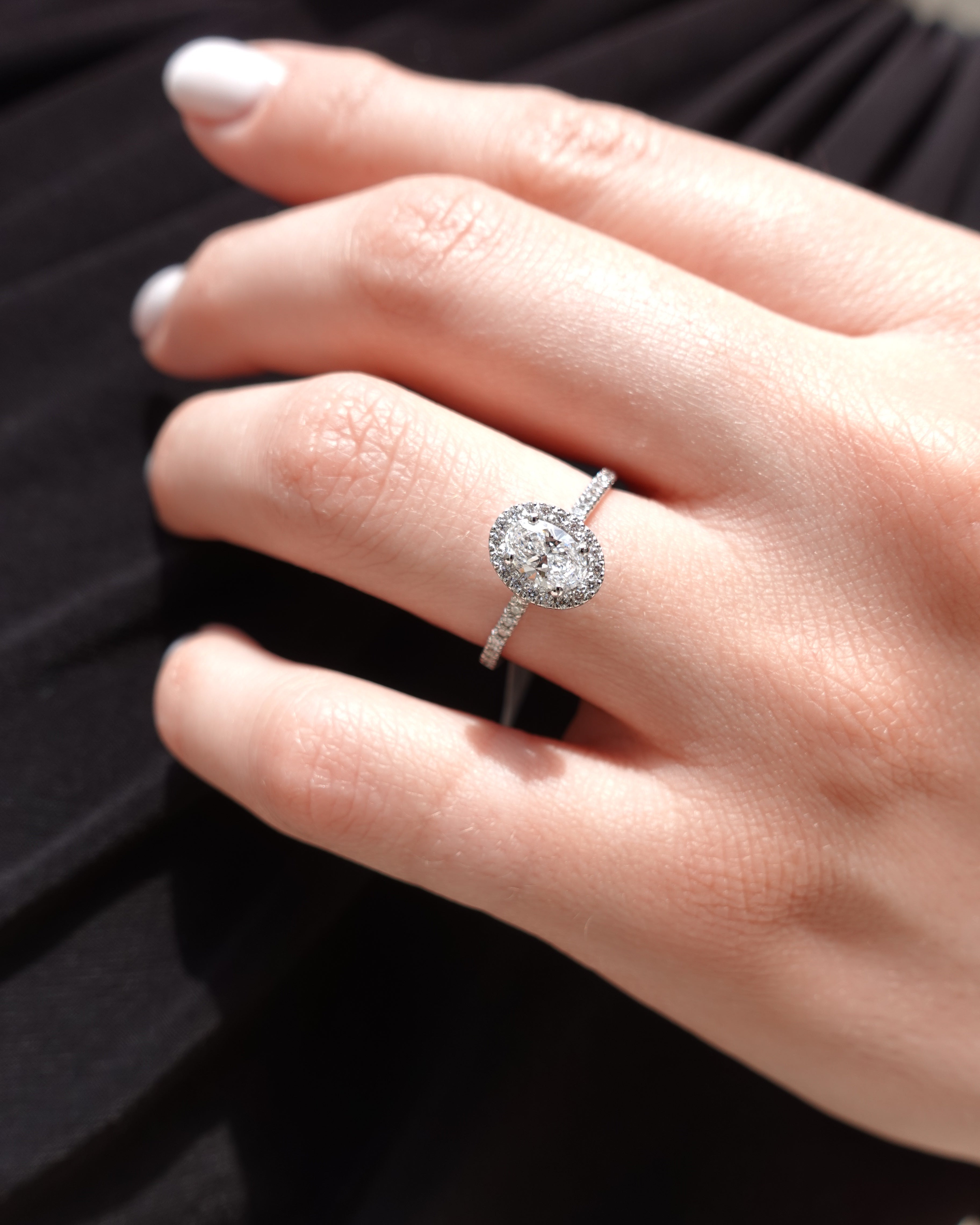Close-up of a hand wearing a oval-cut diamond ring with a blurred background