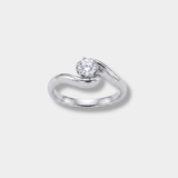 A white-gold engagement ring featuring a round-cut clear gemstone in a curved, flowing band setting, shown on a light gray background.
