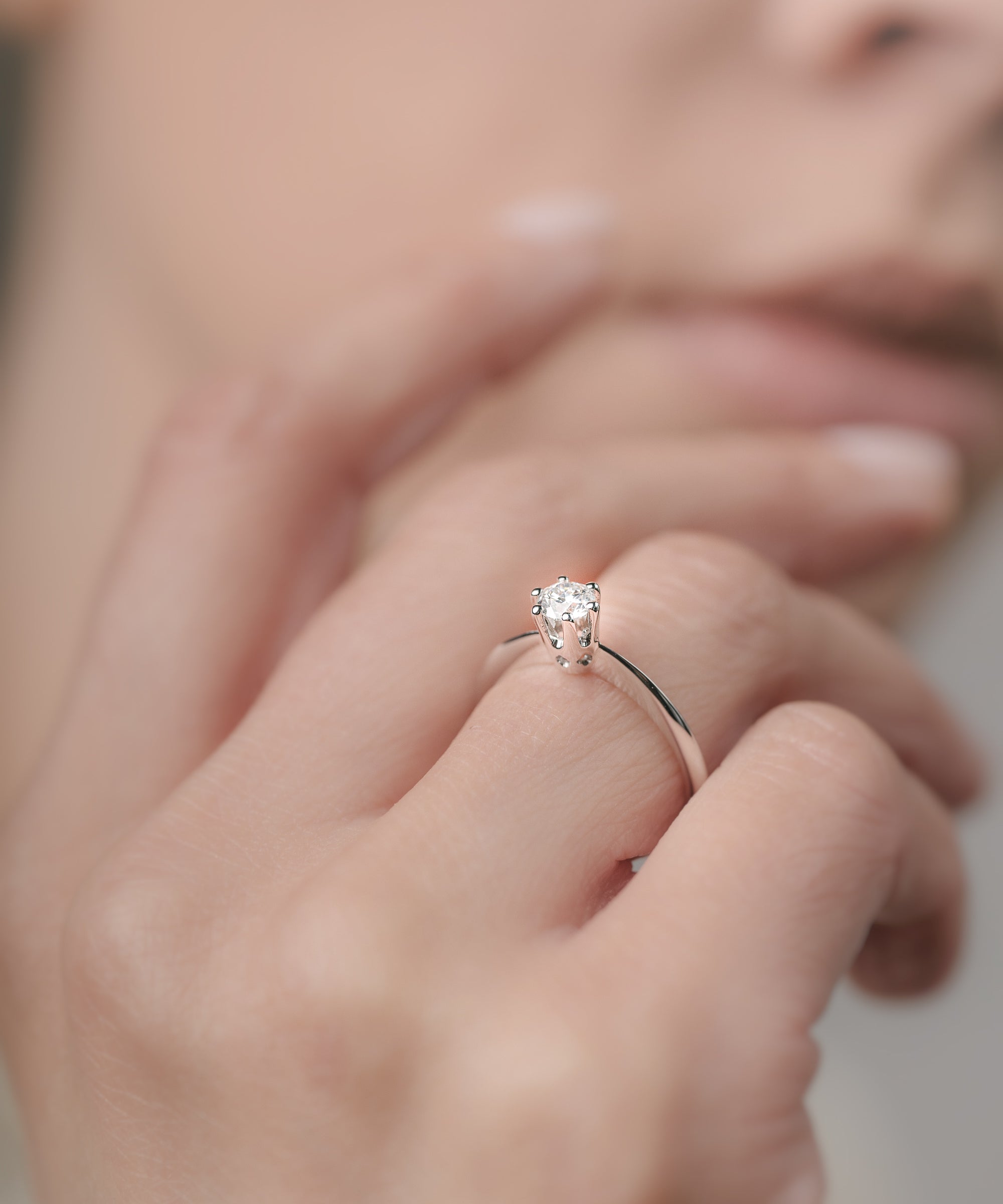 Close-up of a hand wearing a diamond ring with a blurred background