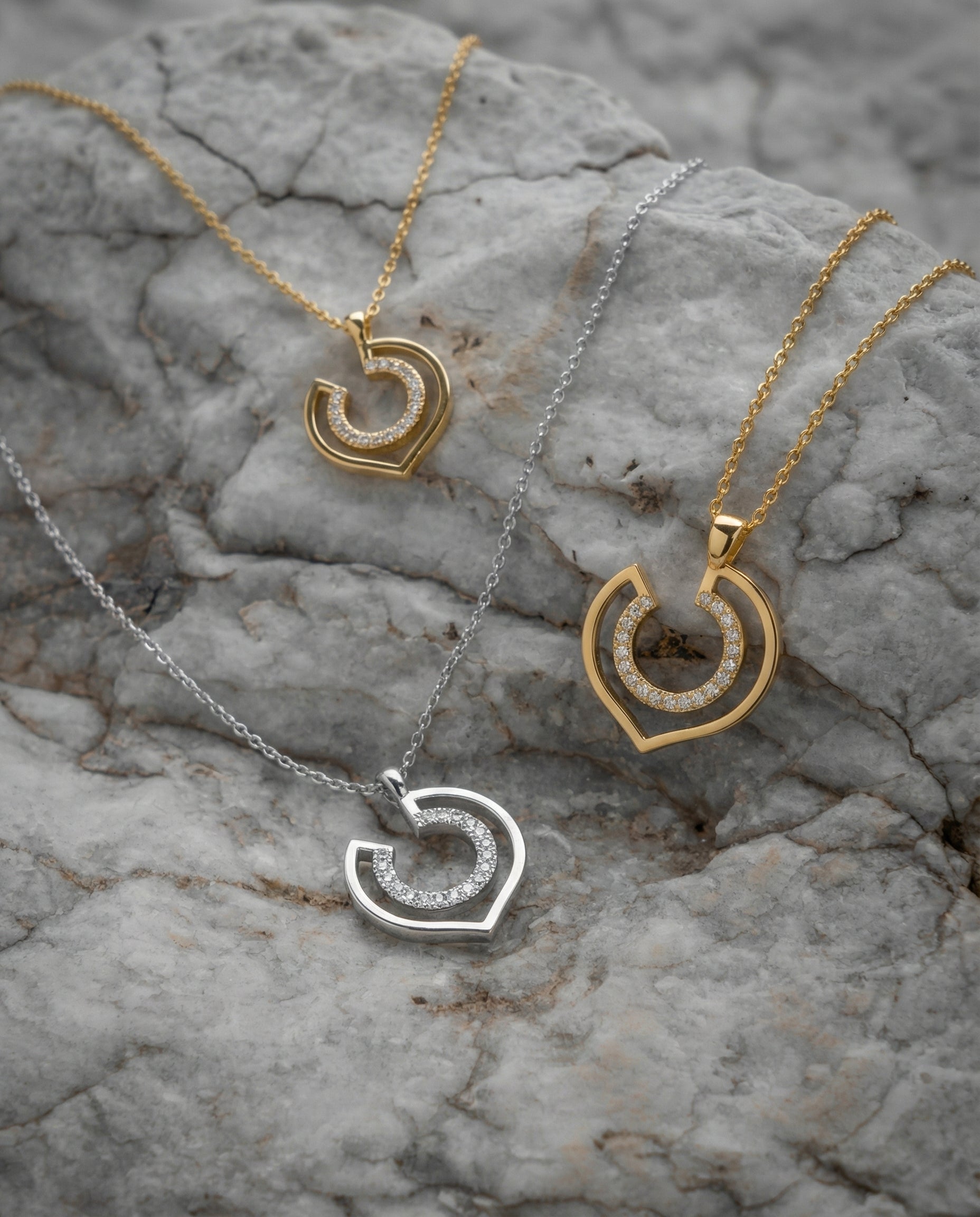 Three geometric necklaces with diamonds over a textured stone surface