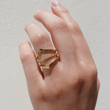 Hand wearing a gold geometric ring on a plain background