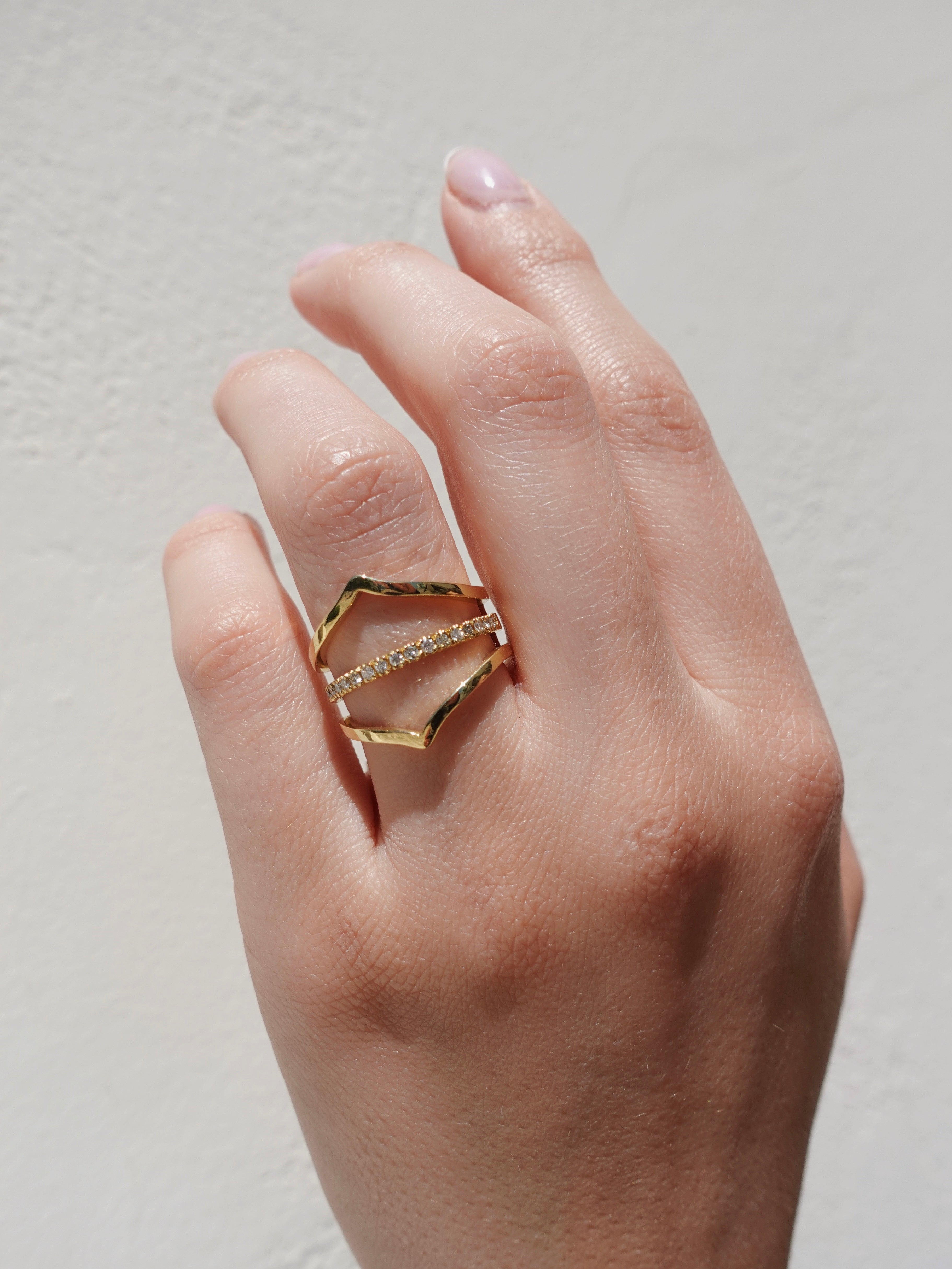 Hand wearing a gold geometric ring on a plain background