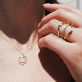 Close-up of a hand wearing a gold ring with a pendant necklace.