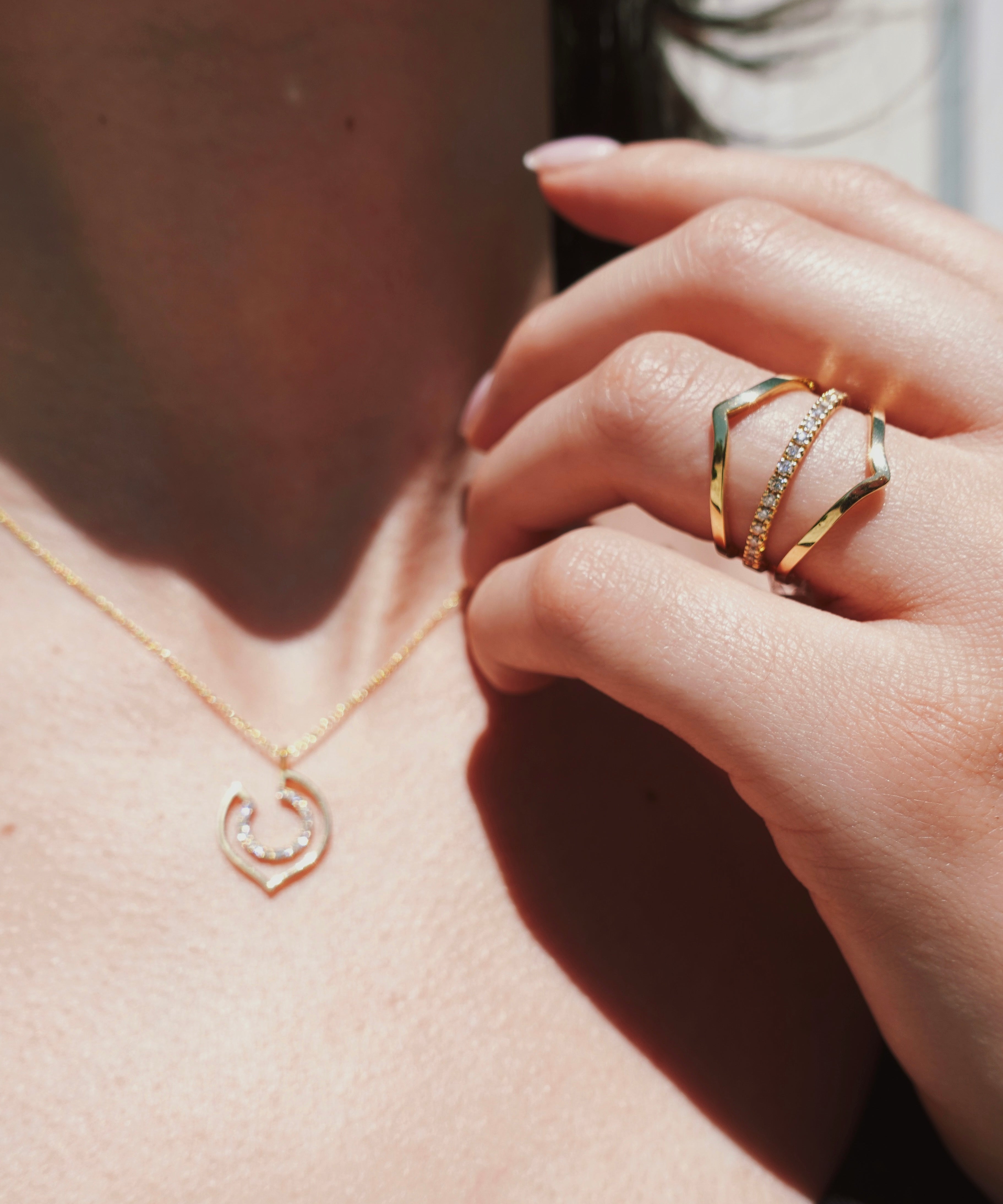 Close-up of a hand wearing a gold ring with a pendant necklace.