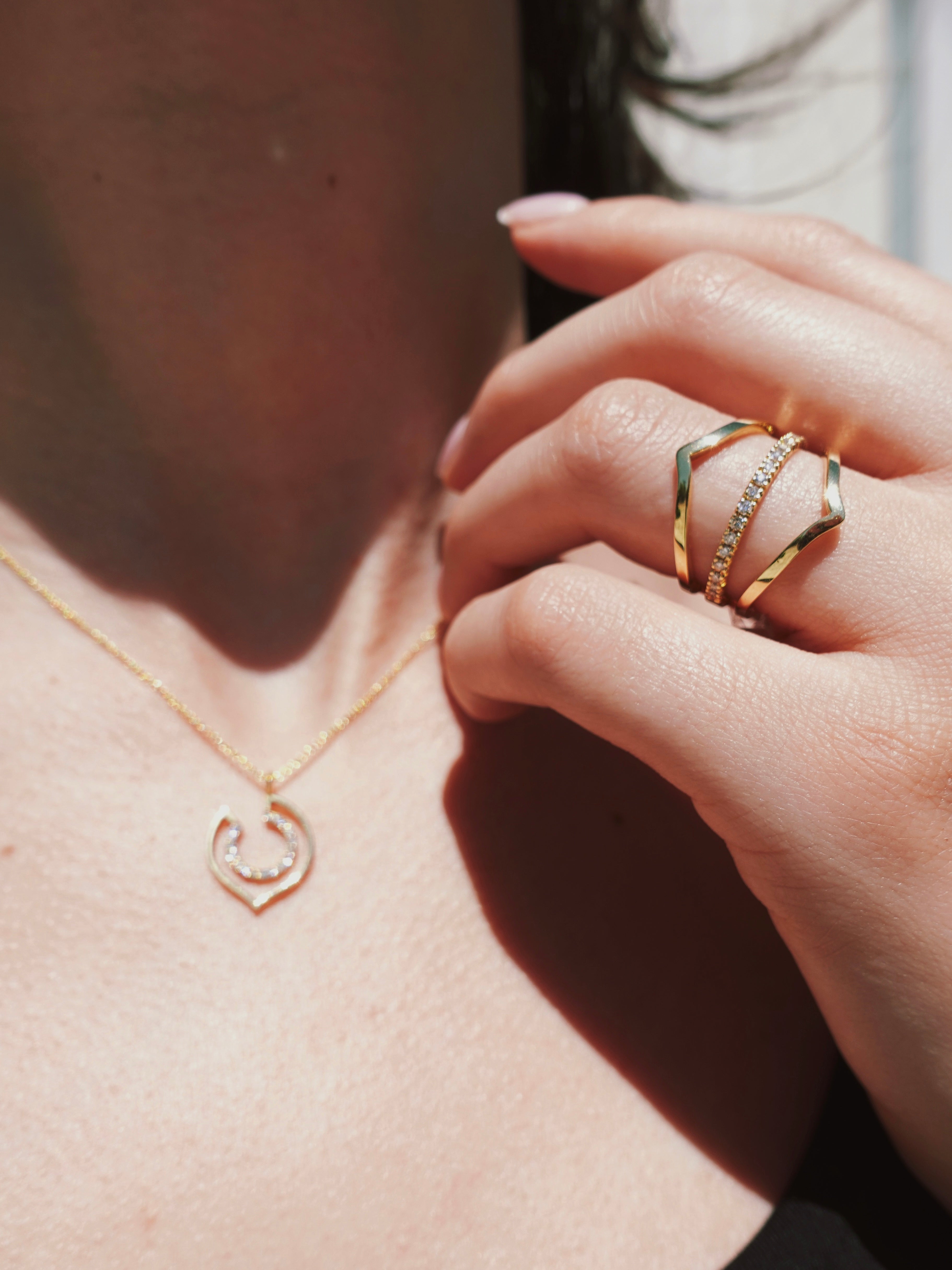 Close-up of a hand wearing a gold ring with a pendant necklace.
