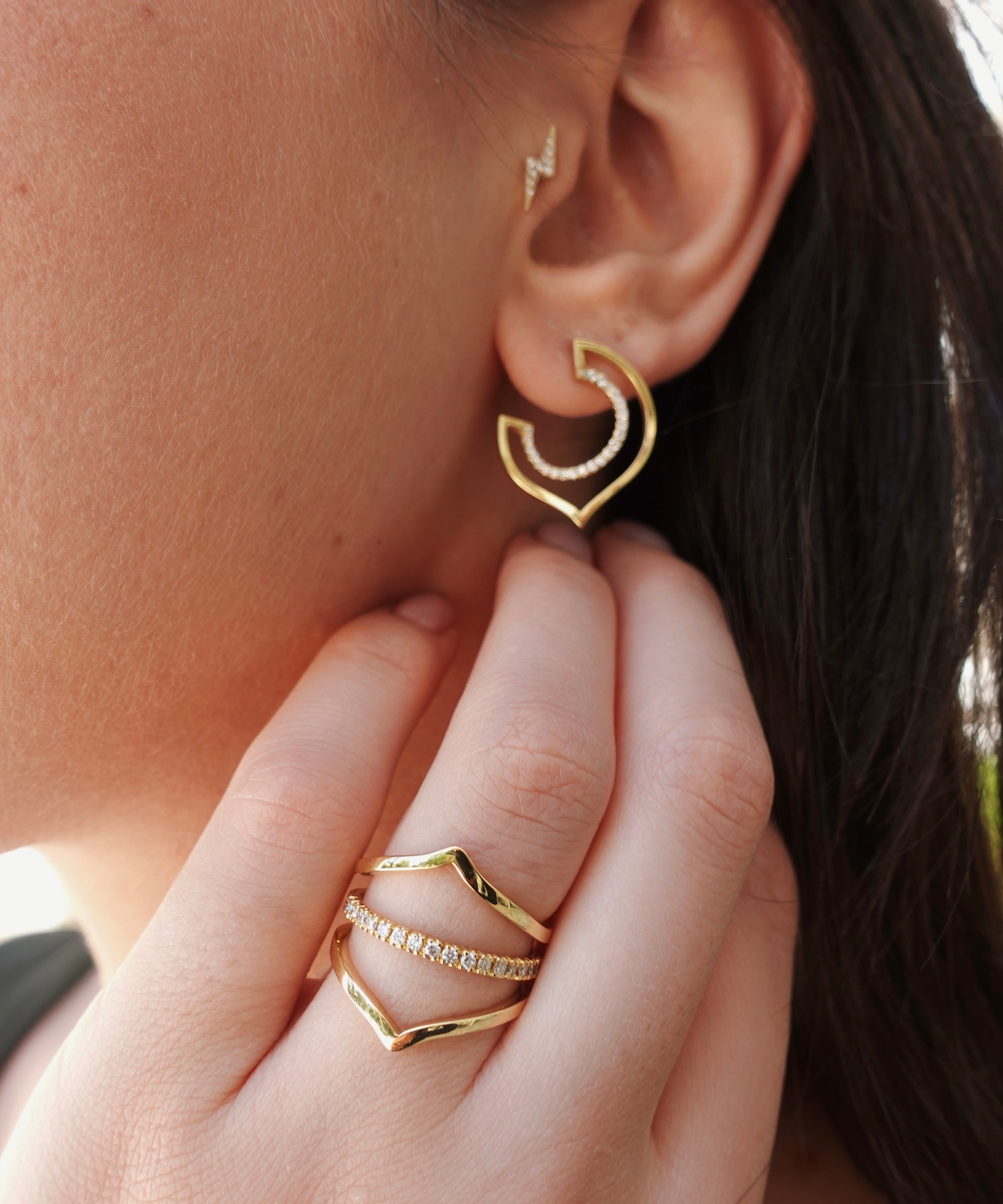 Gold hoop earrings being worn with a hand adjusting them.