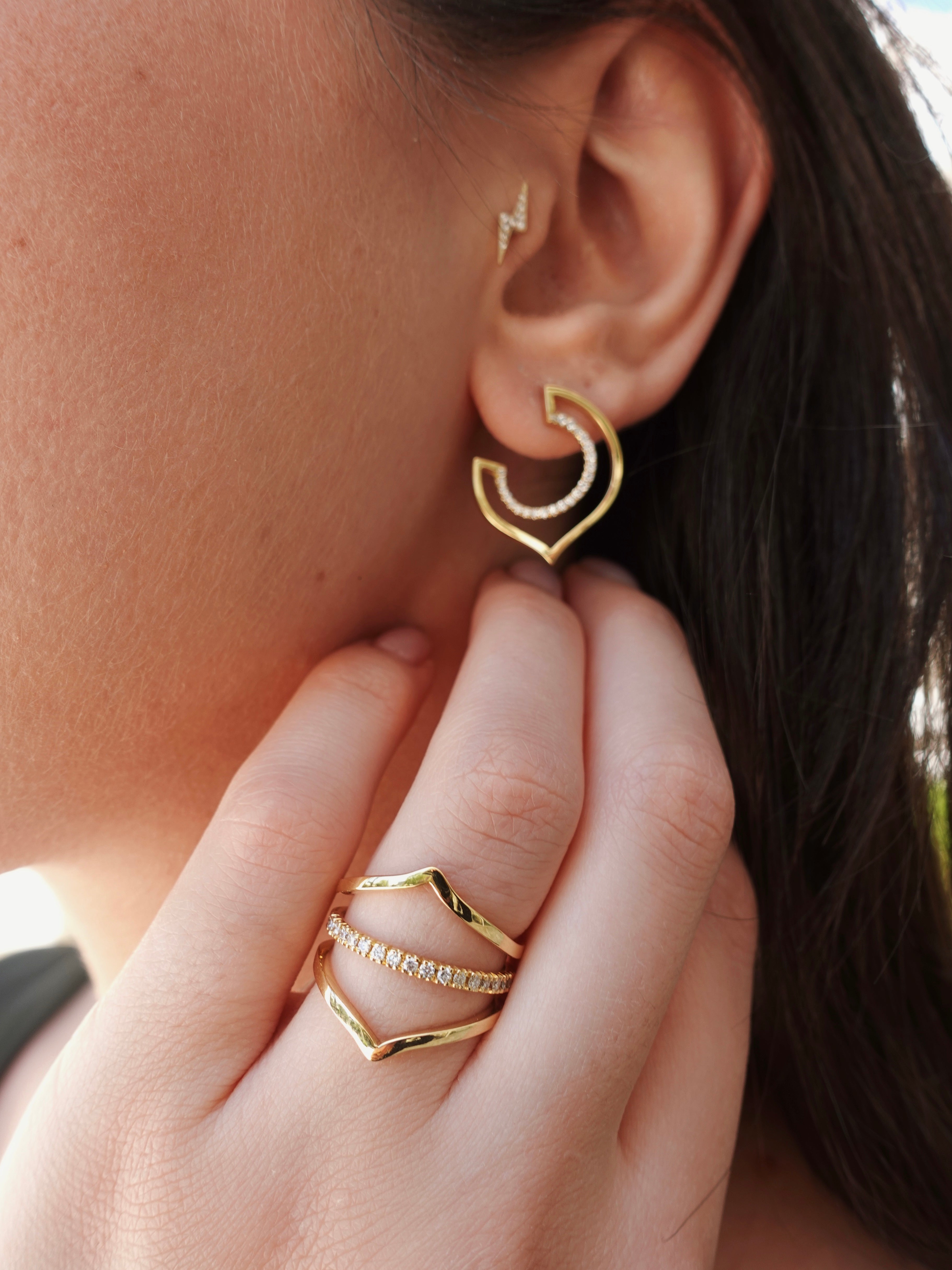 Gold hoop earrings being worn with a hand adjusting them.