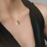 Gold necklace with a pendant on a person wearing a black top against a neutral background