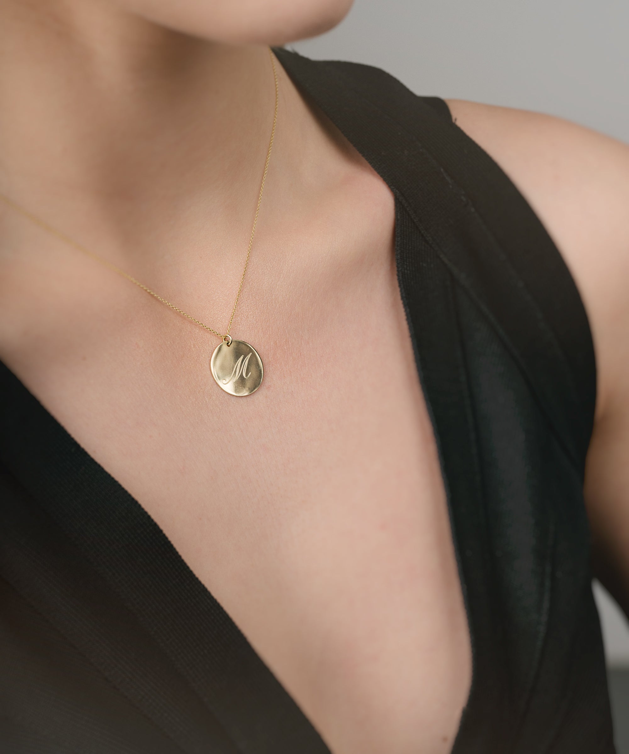 Gold necklace with a pendant on a person wearing a black top against a neutral background