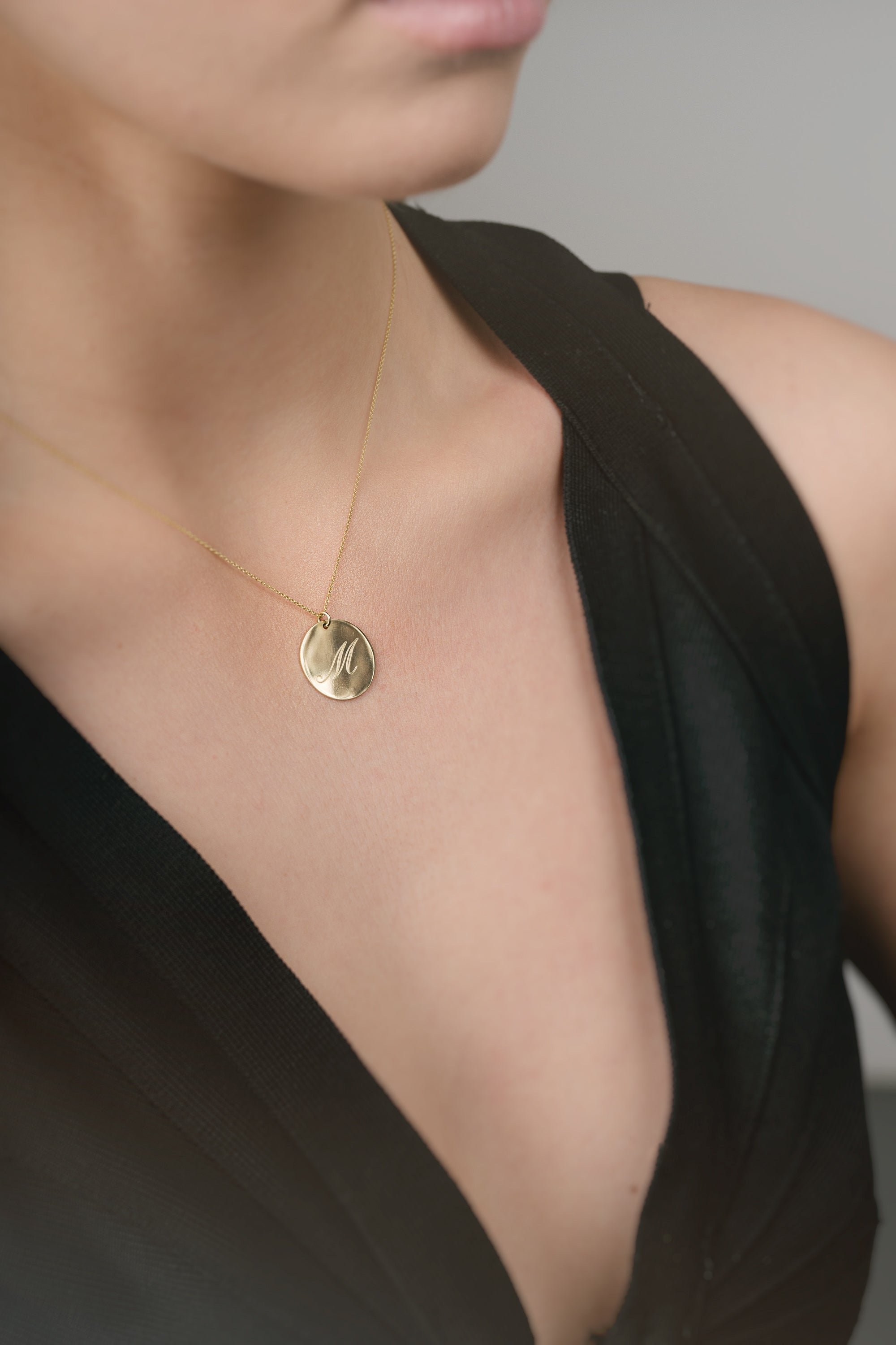 Gold necklace with a pendant on a person wearing a black top against a neutral background