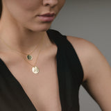 Woman wearing a black sleeveless top with gold necklaces on a neutral background