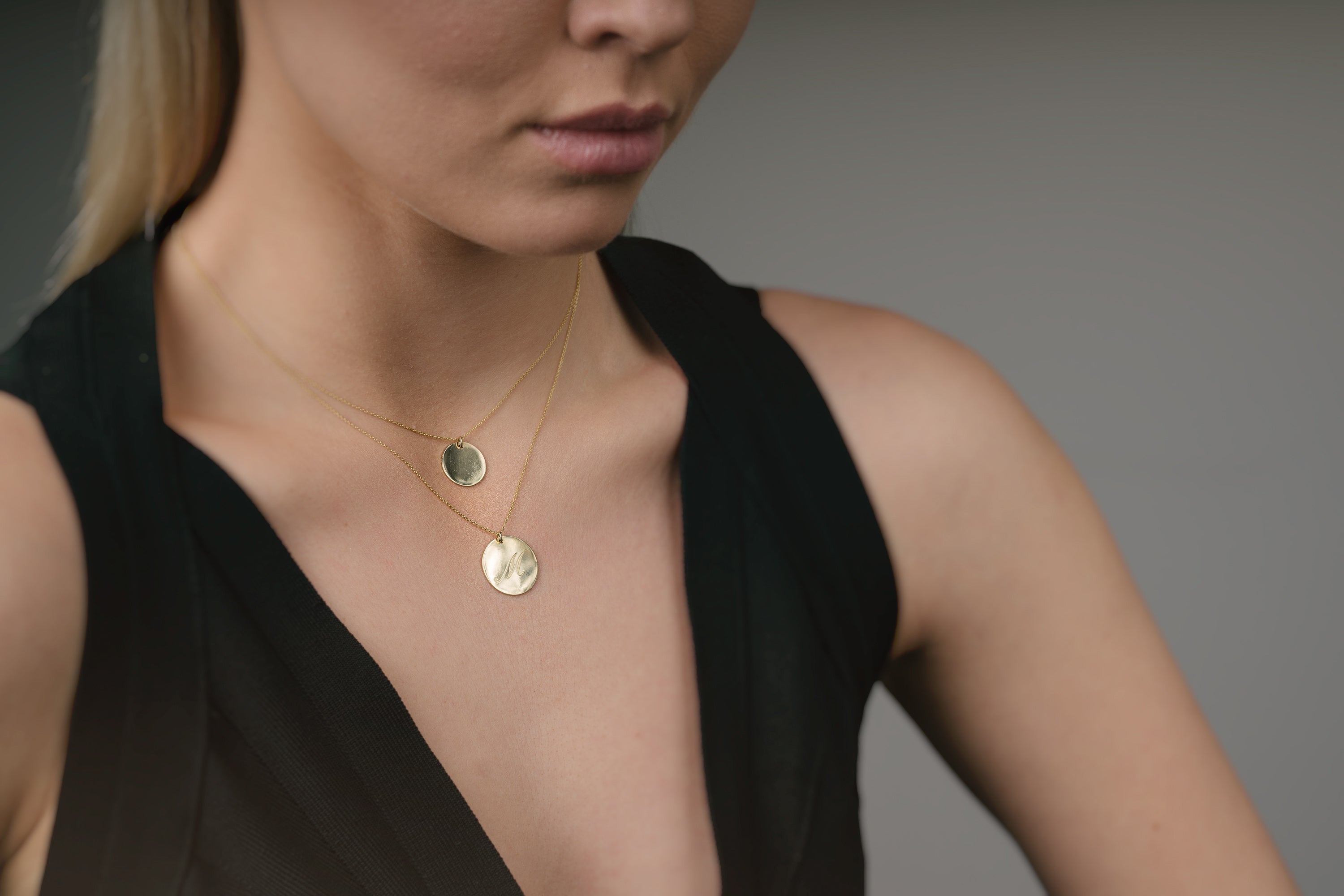 Woman wearing a black sleeveless top with gold necklaces on a neutral background