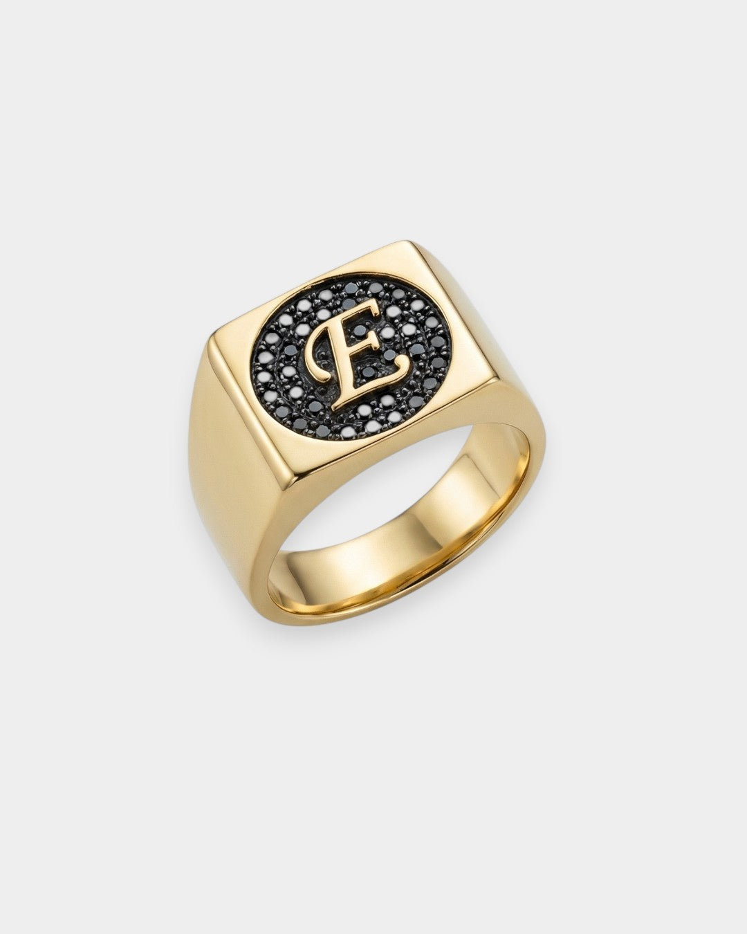 Gold ring with letter 'E' and black stones on a white background
