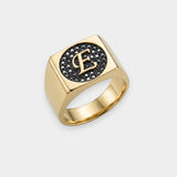 Gold ring with letter 'E' and black stones on a white background