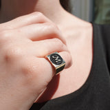 Close-up of a hand wearing a gold ring with black diamonds on a blurred background