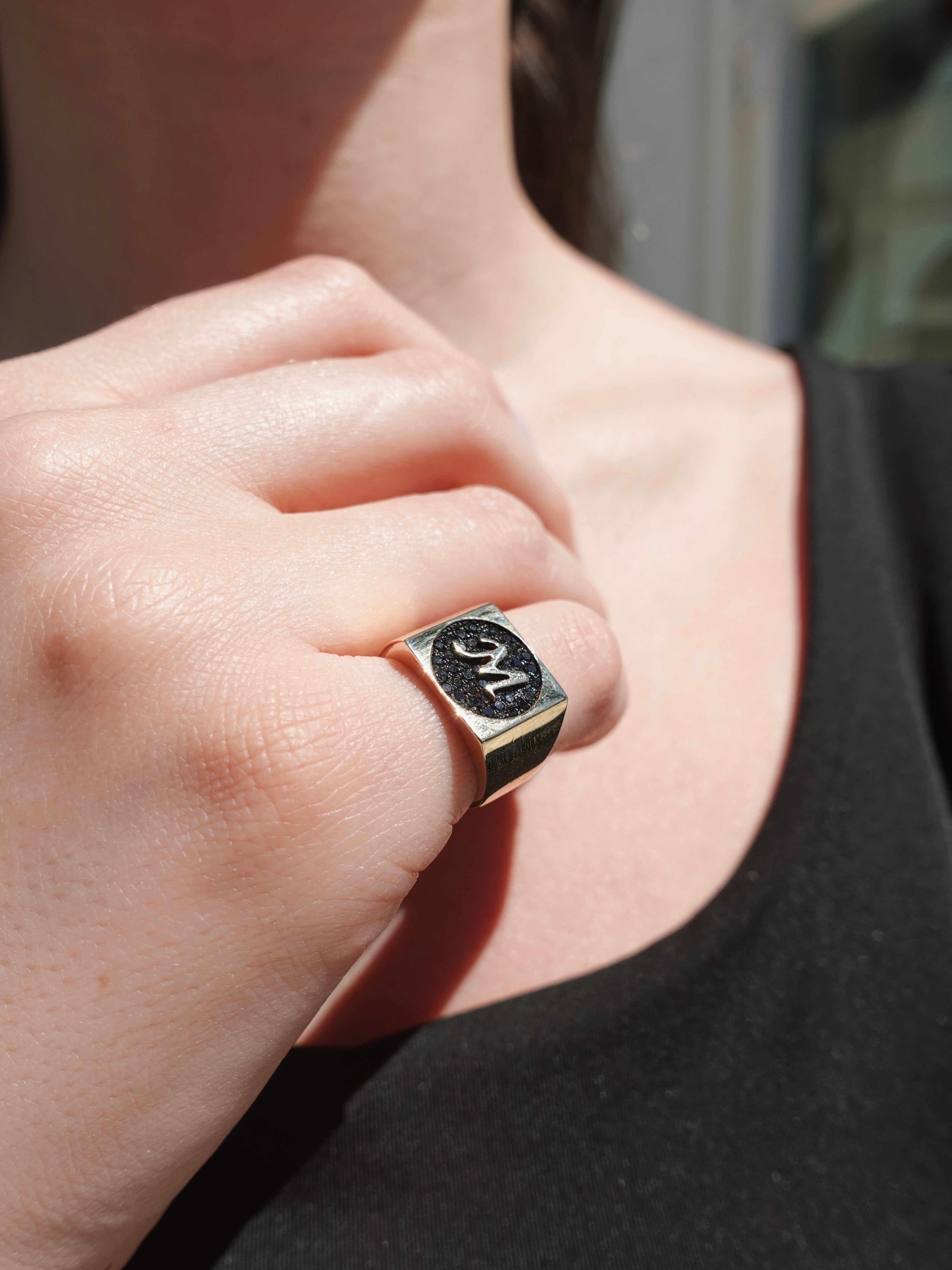 Close-up of a hand wearing a gold ring with black diamonds on a blurred background